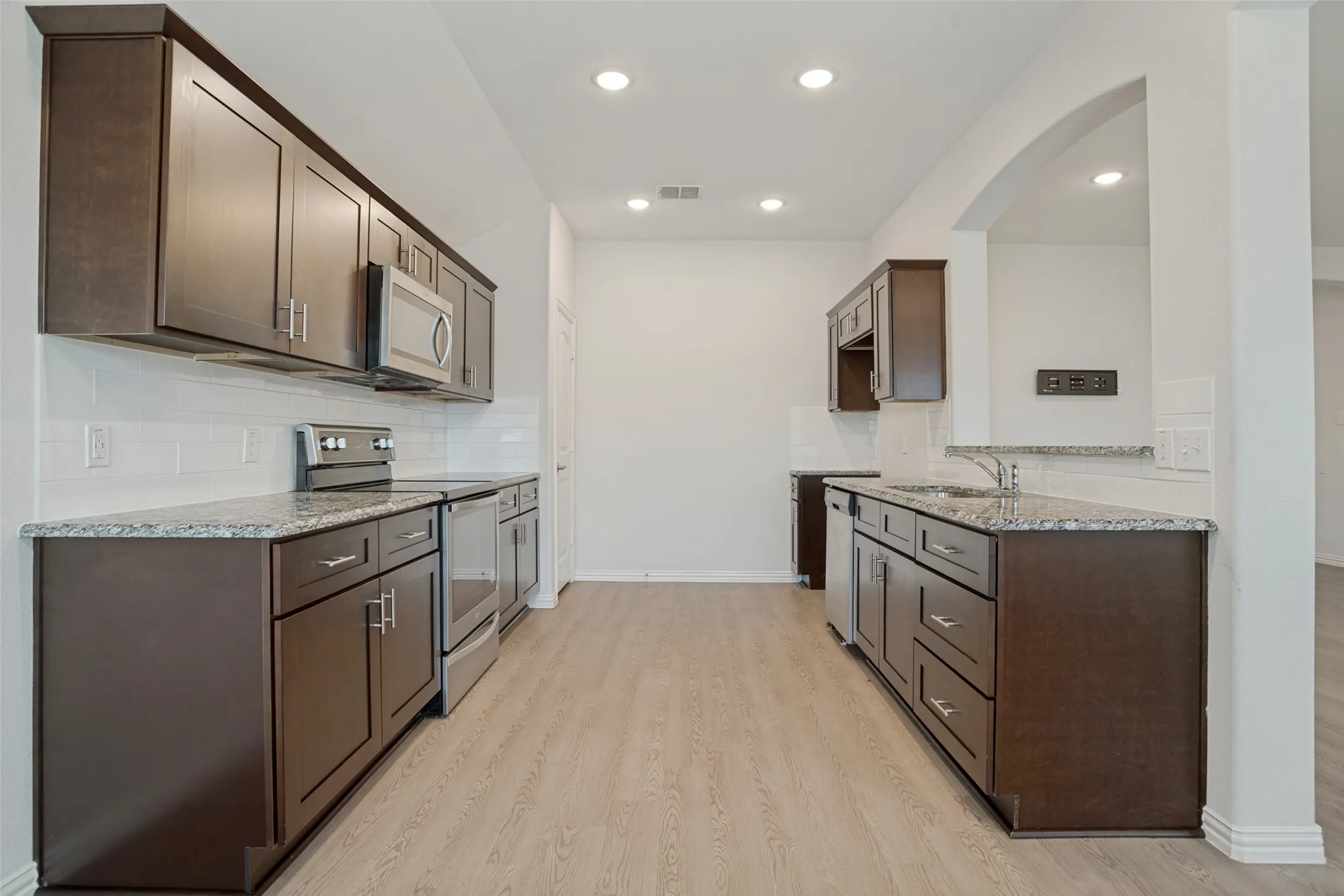 Dark wood-finish cabinetry, speckled countertops, stainless steel appliances, white subway tile backsplash, and LVP flooring