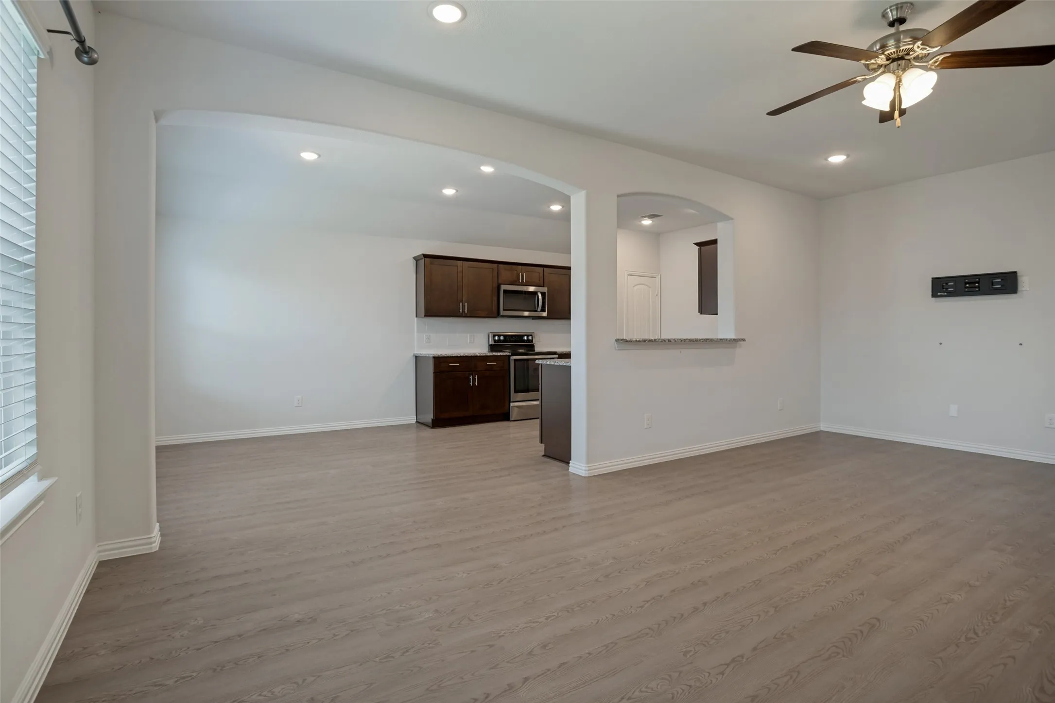 recessed lighting, arched doorways, a ceiling fan with integrated lighting, and a kitchen featuring dark wood cabinetry and stainless steel appliances