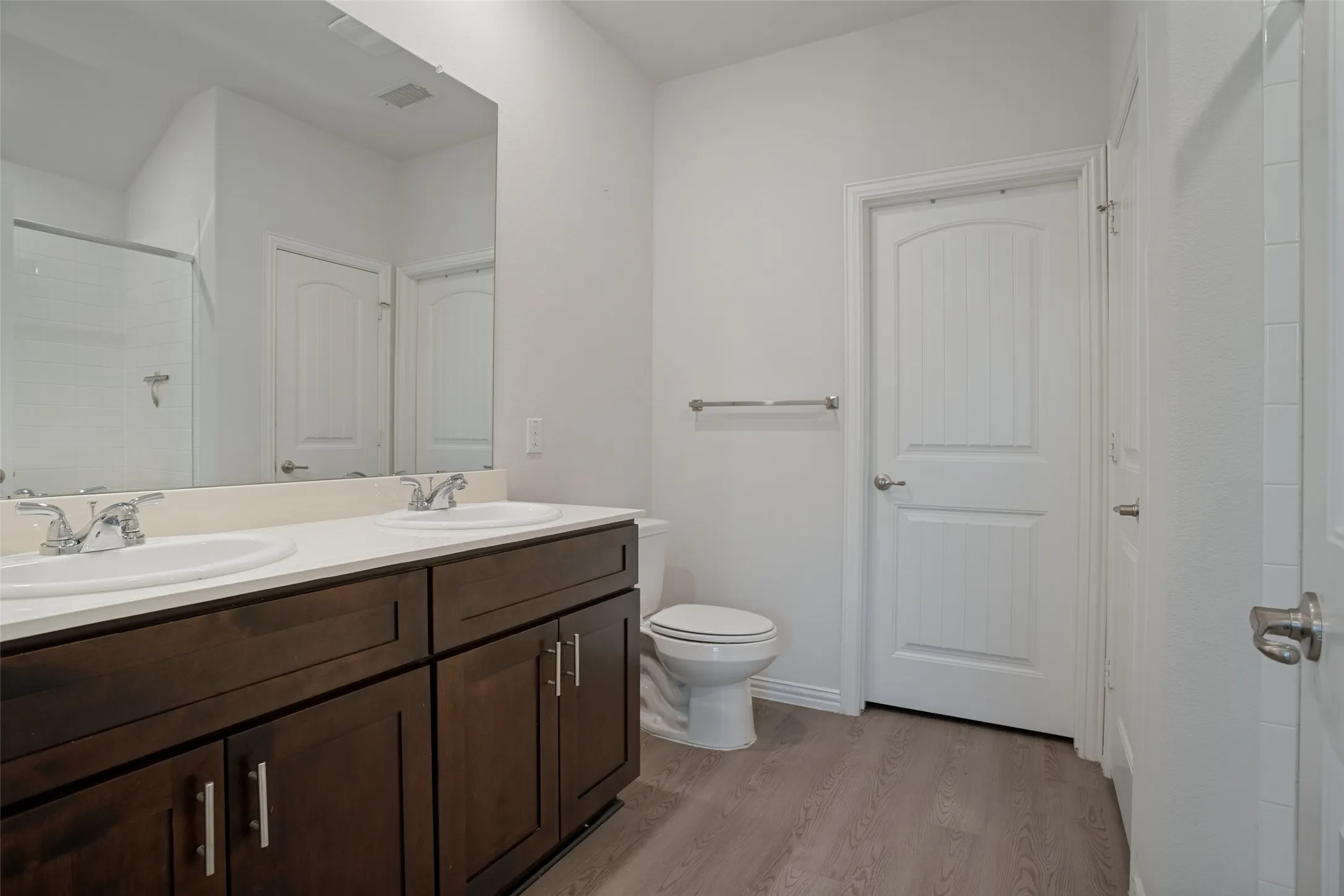 Dual vanity with undermount sinks, wood-finish cabinetry, and a large wall-mounted mirror