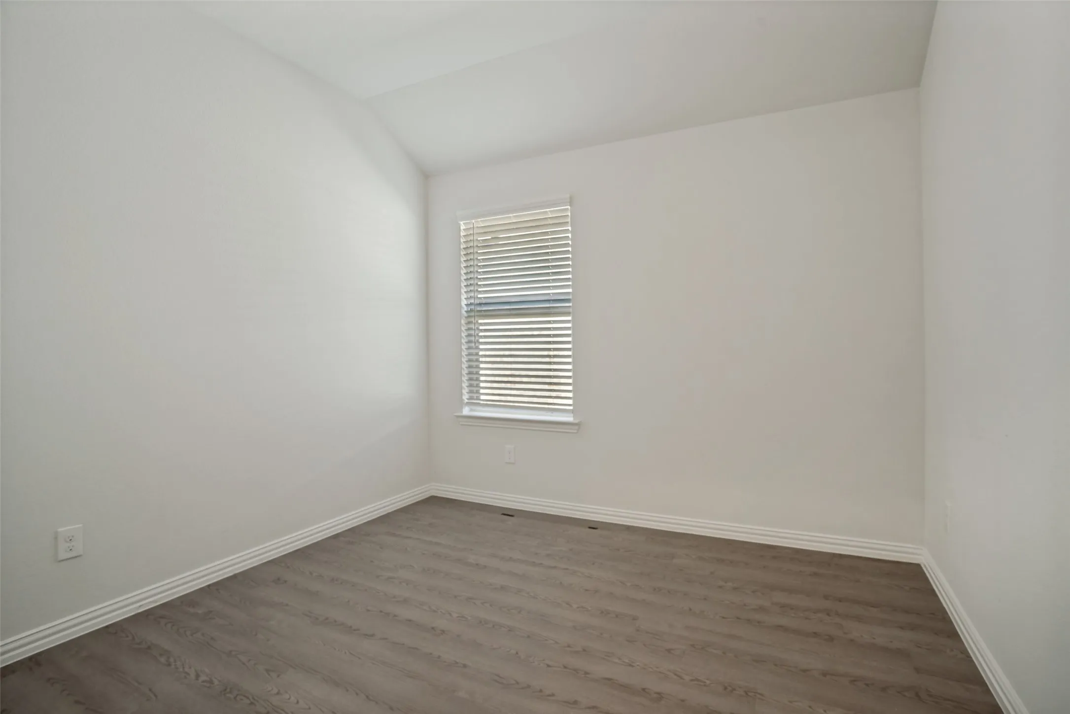 Bright bedroom featuring neutral wall finishes, LVP flooring, and a large window with plantation shutters providing natural light and privacy control