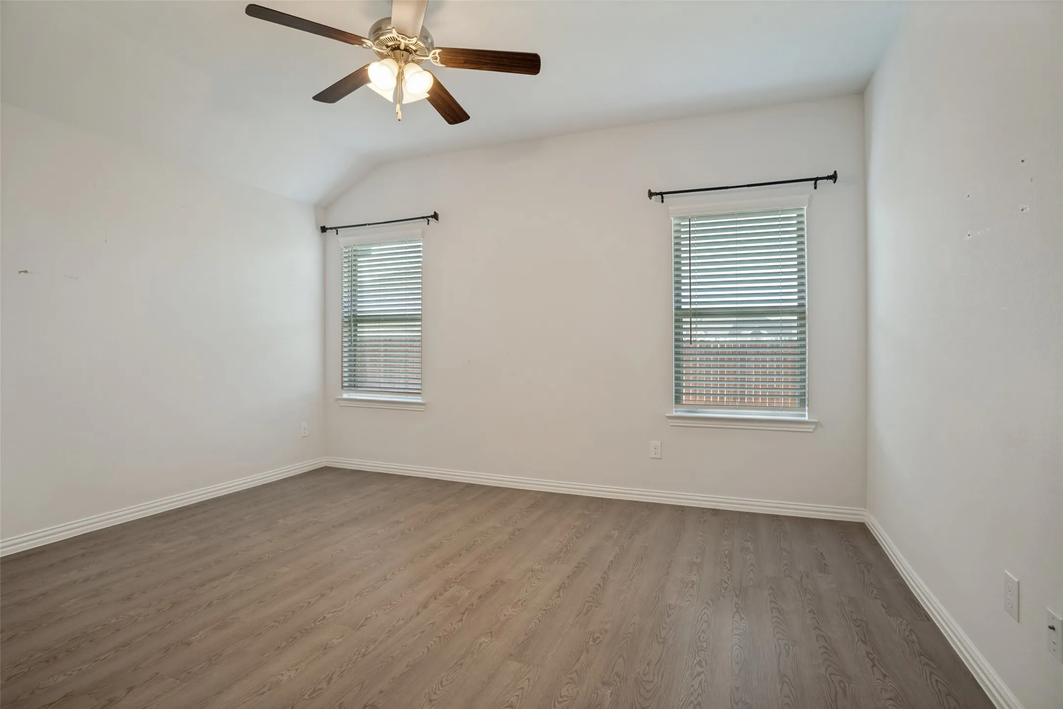 Vaulted ceiling with a ceiling fan, two windows with blinds and curtain rods, and LVP flooring
