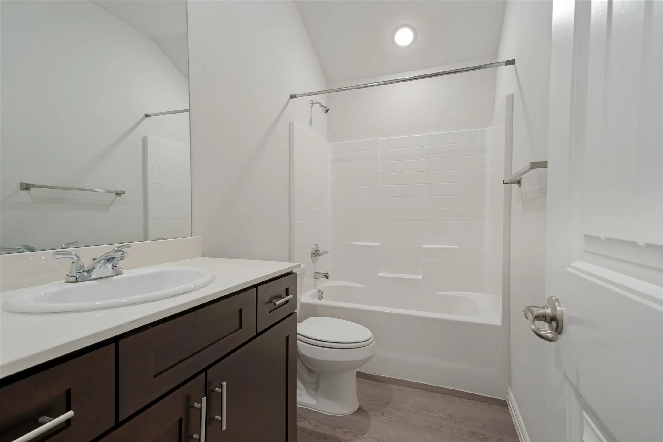 Bathroom featuring a bathtub with shower, white tile surround, dark wood-finish vanity with a white countertop, and wood-finish flooring