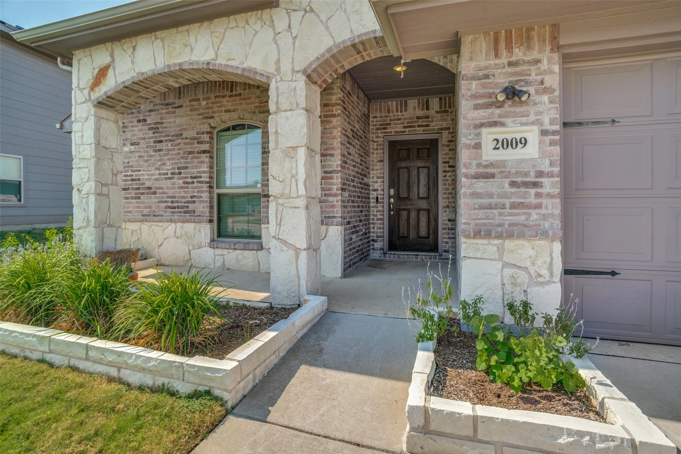 Brick and stone facade with arched entryways, integrated garage, and a paneled entry door