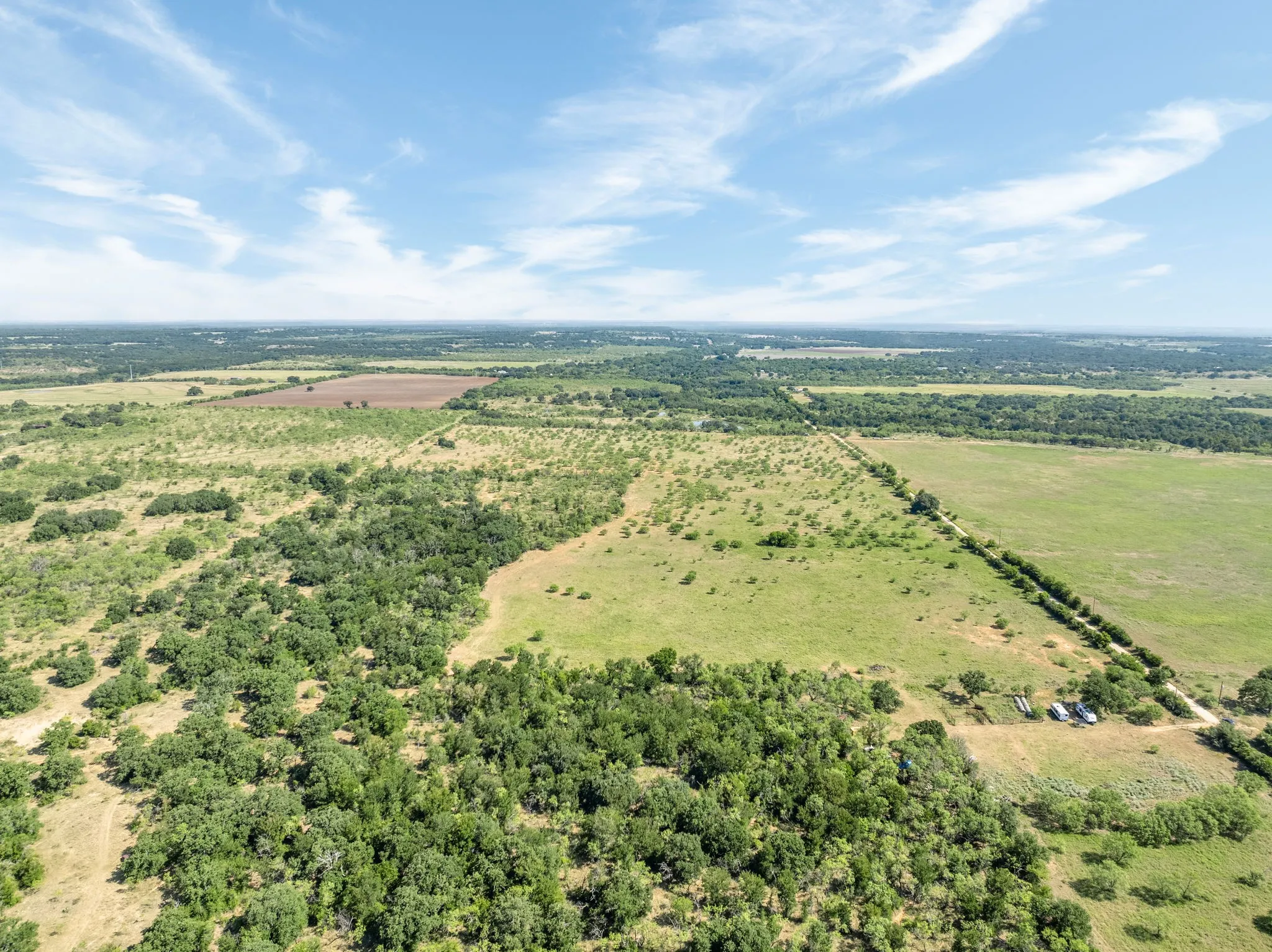 Expansive rural landscape featuring a mix of open fields, wooded areas, and distant agricultural land