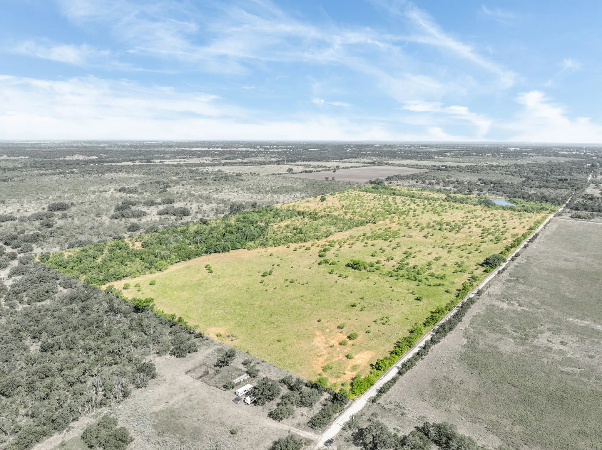 Expansive land parcel featuring open fields, scattered mature trees, and a visible roadway