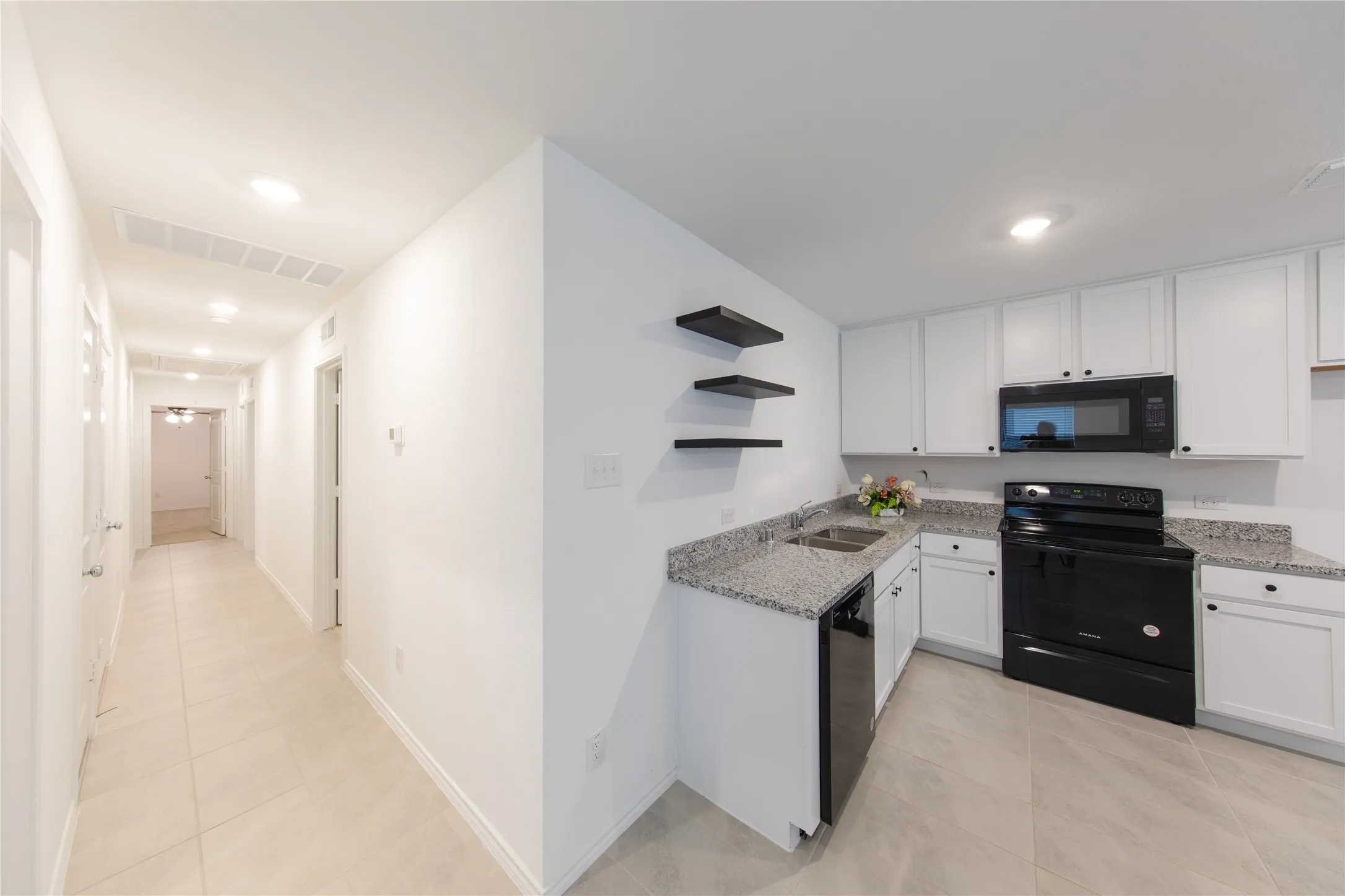 Kitchen featuring sink, white cabinetry, light tile floors, and black appliances