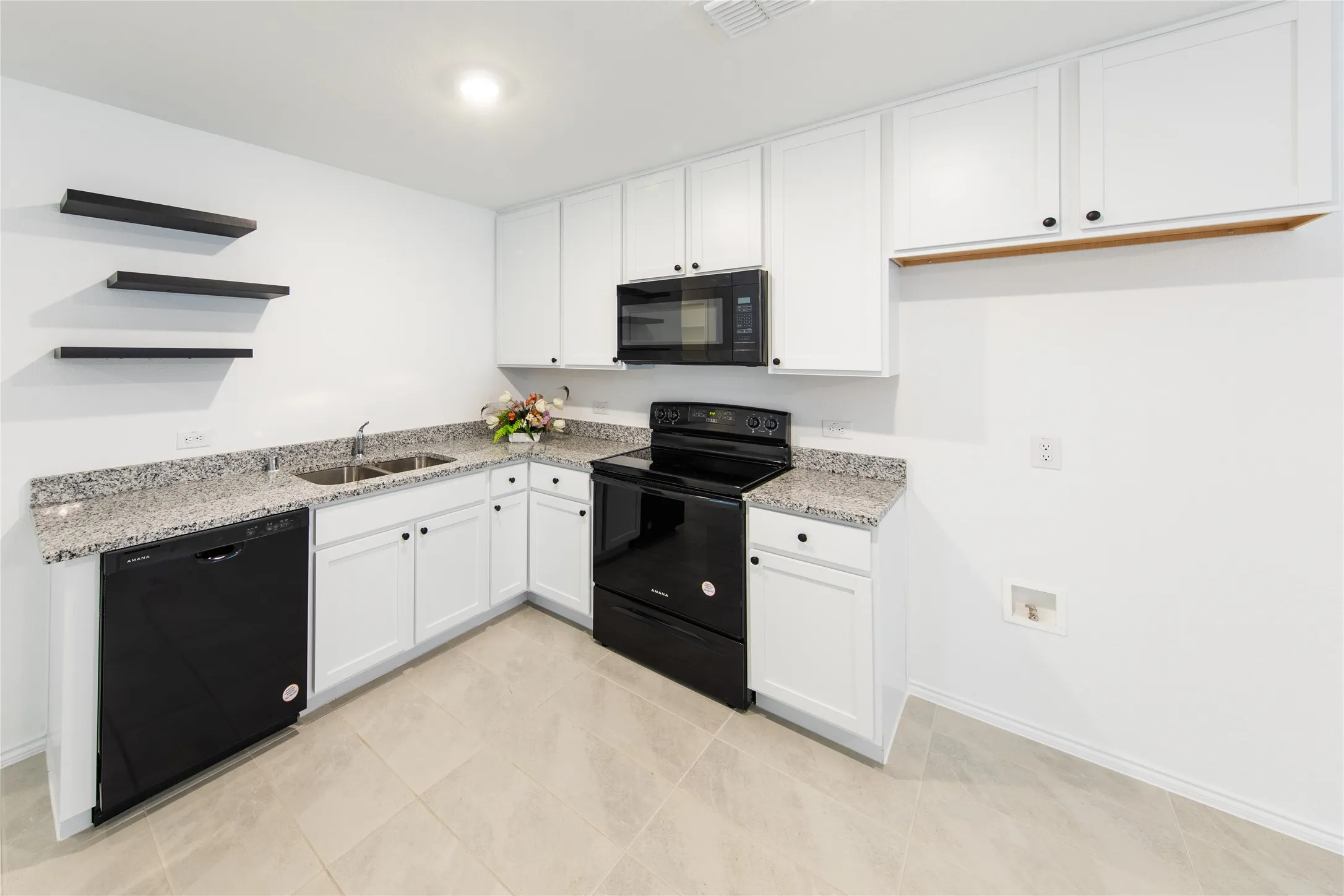 Kitchen with black appliances, light stone counters, white cabinets, sink, and light tile floors