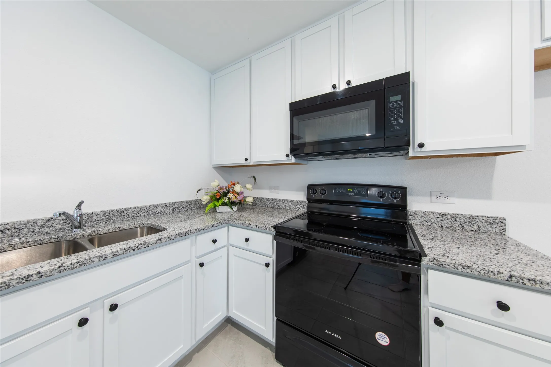 Kitchen featuring white cabinets, light tile flooring, light stone countertops, black appliances, and sink