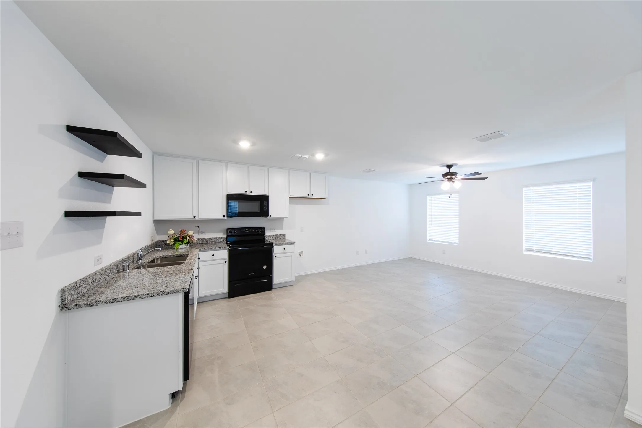 Kitchen with ceiling fan, black appliances, light stone counters, white cabinets, and sink