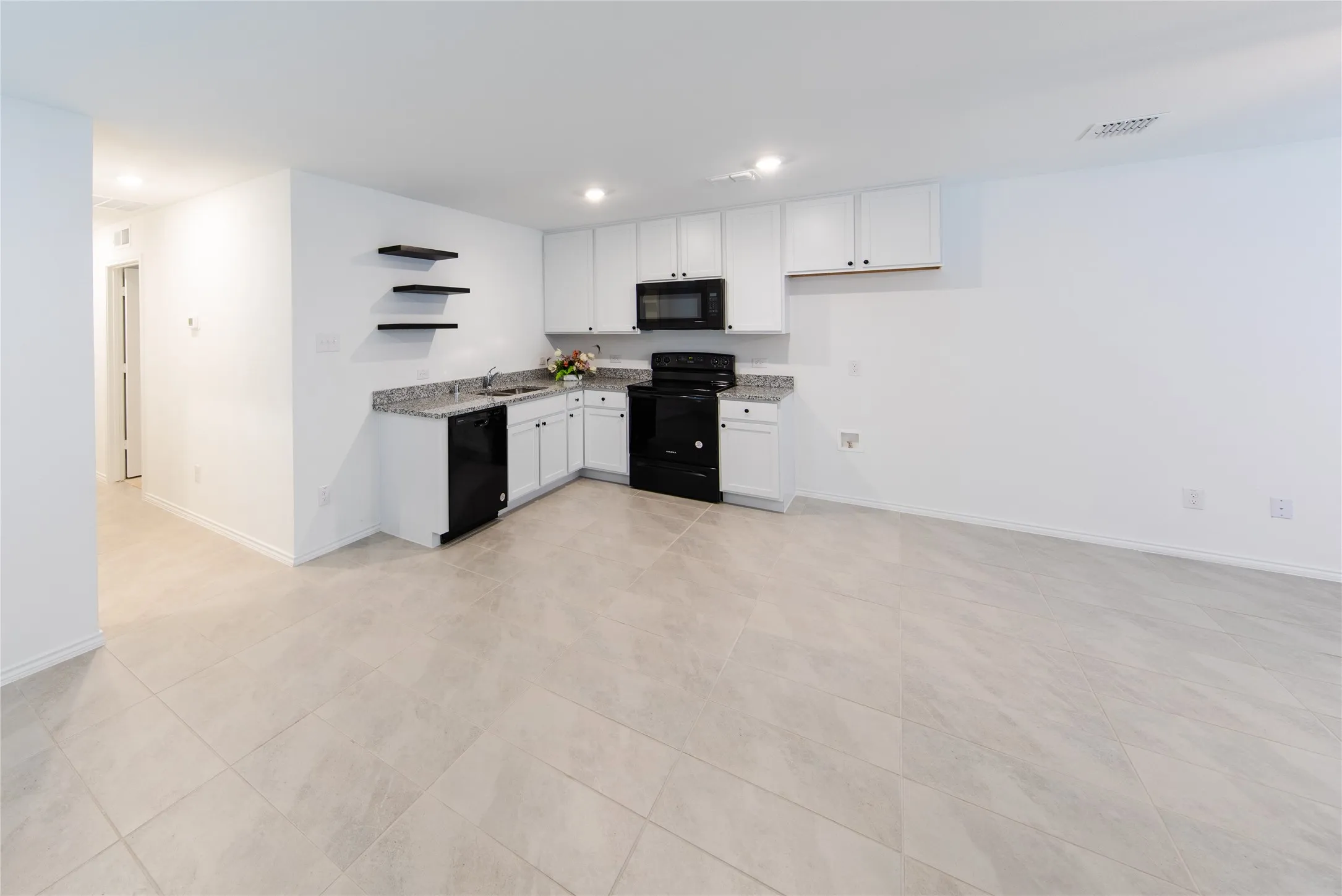 Kitchen with white cabinets, light tile flooring, black appliances, sink, and light stone counters