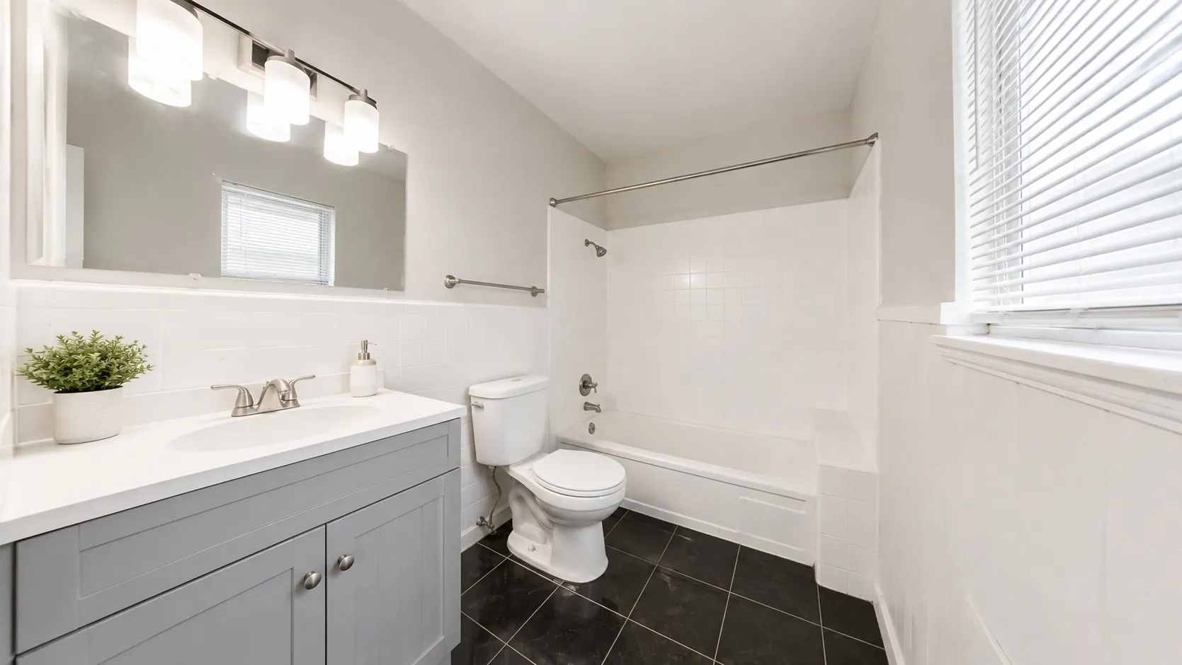 Bathroom with a single vanity, white countertop, gray cabinetry, black floor tiles, and a shower-tub combination