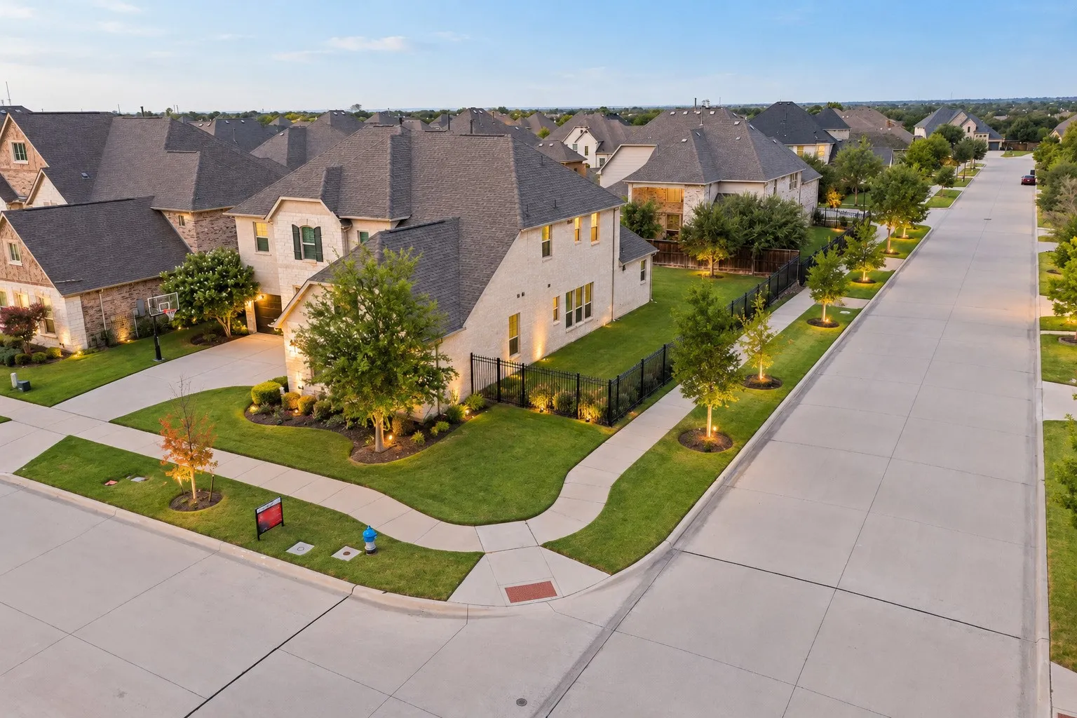 Architectural brick and stone facade, gabled roofs, manicured lawns, paved sidewalks, and mature trees
