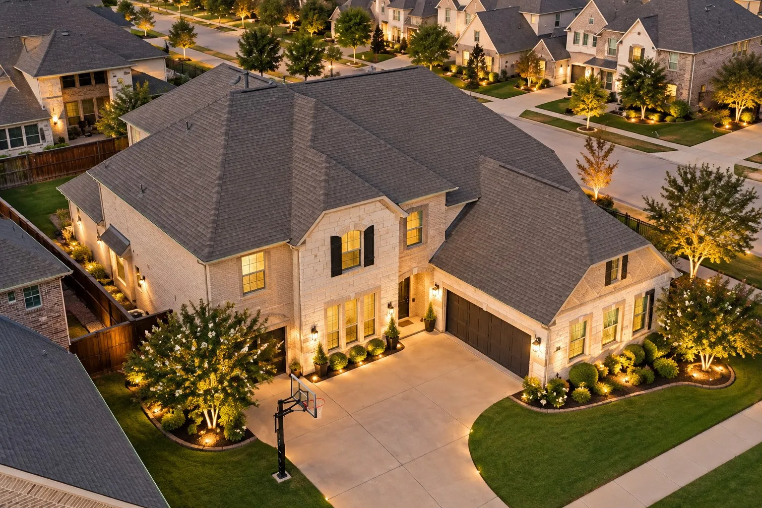Stone exterior with dark shingle roof, attached garage, well-maintained lawn, and established landscaping