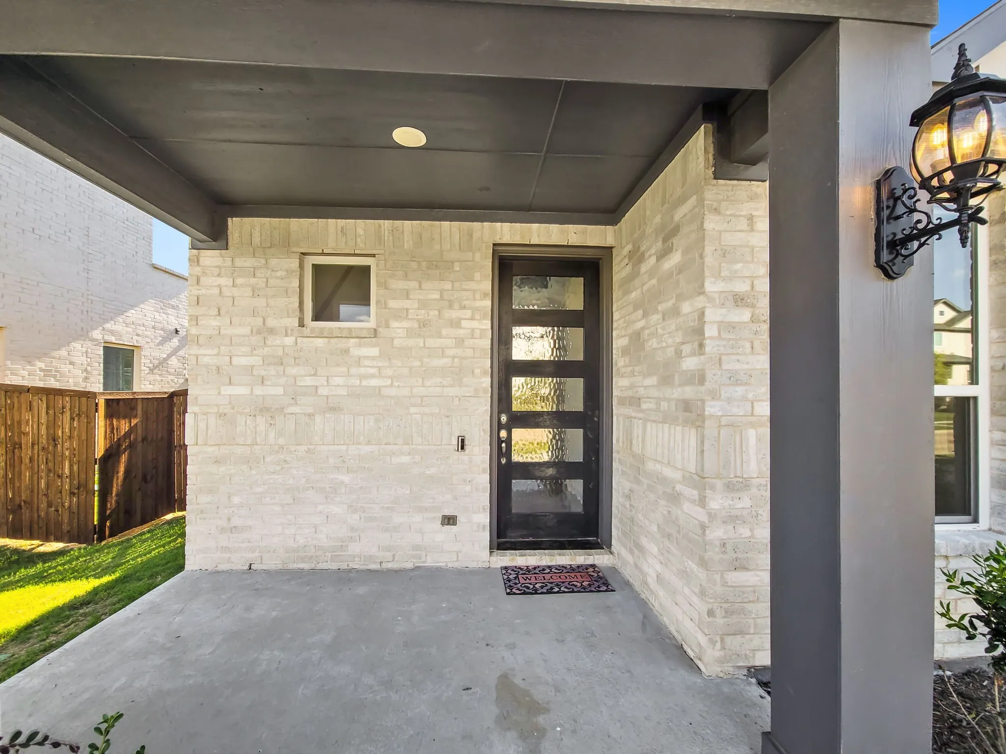 Covered front entry featuring light brick facade, black modern door with textured glass panels, and an ornate wall sconce