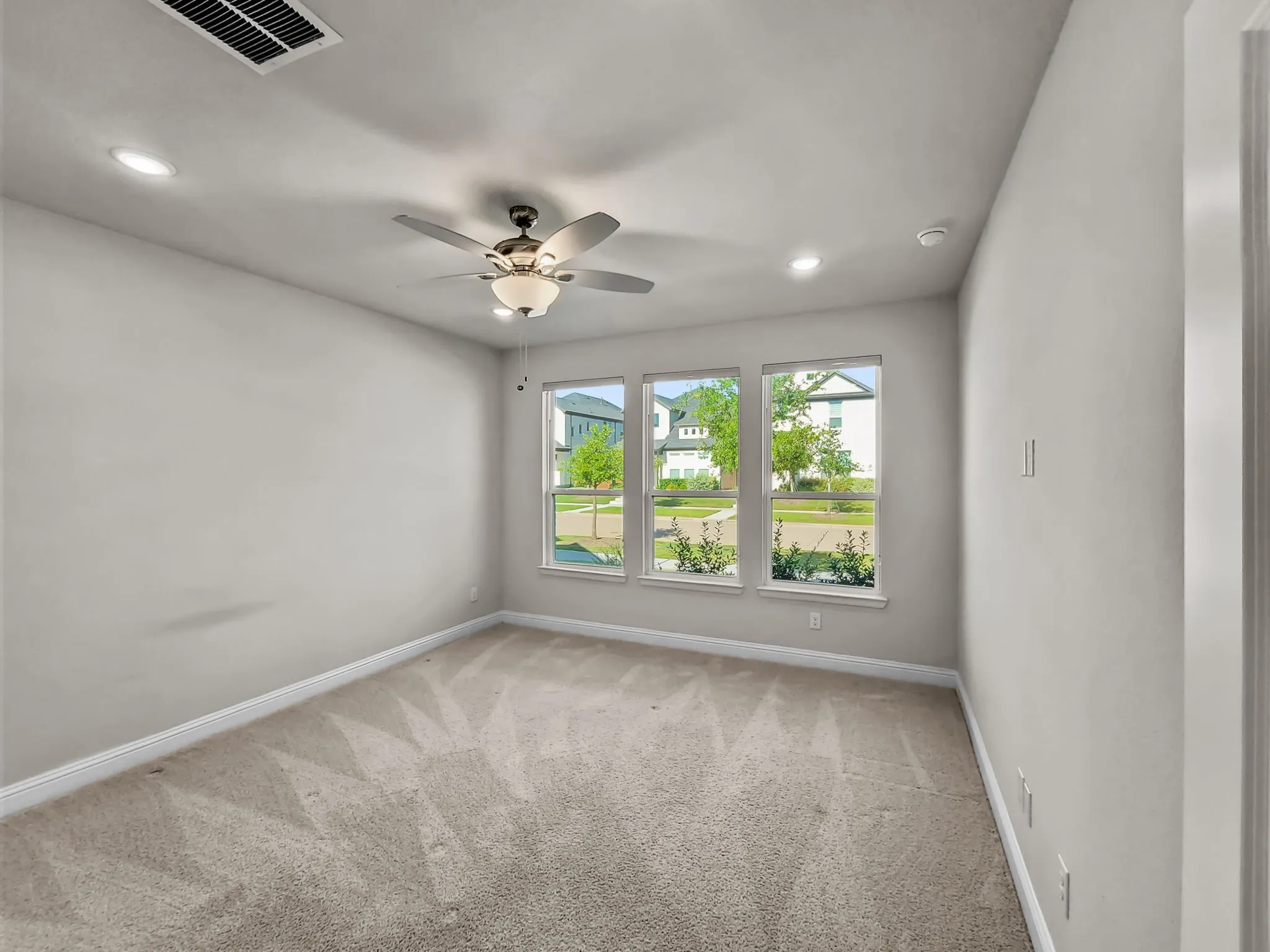 Recessed lighting, ceiling fan with integrated light fixture, light neutral wall color, carpet flooring, three large windows