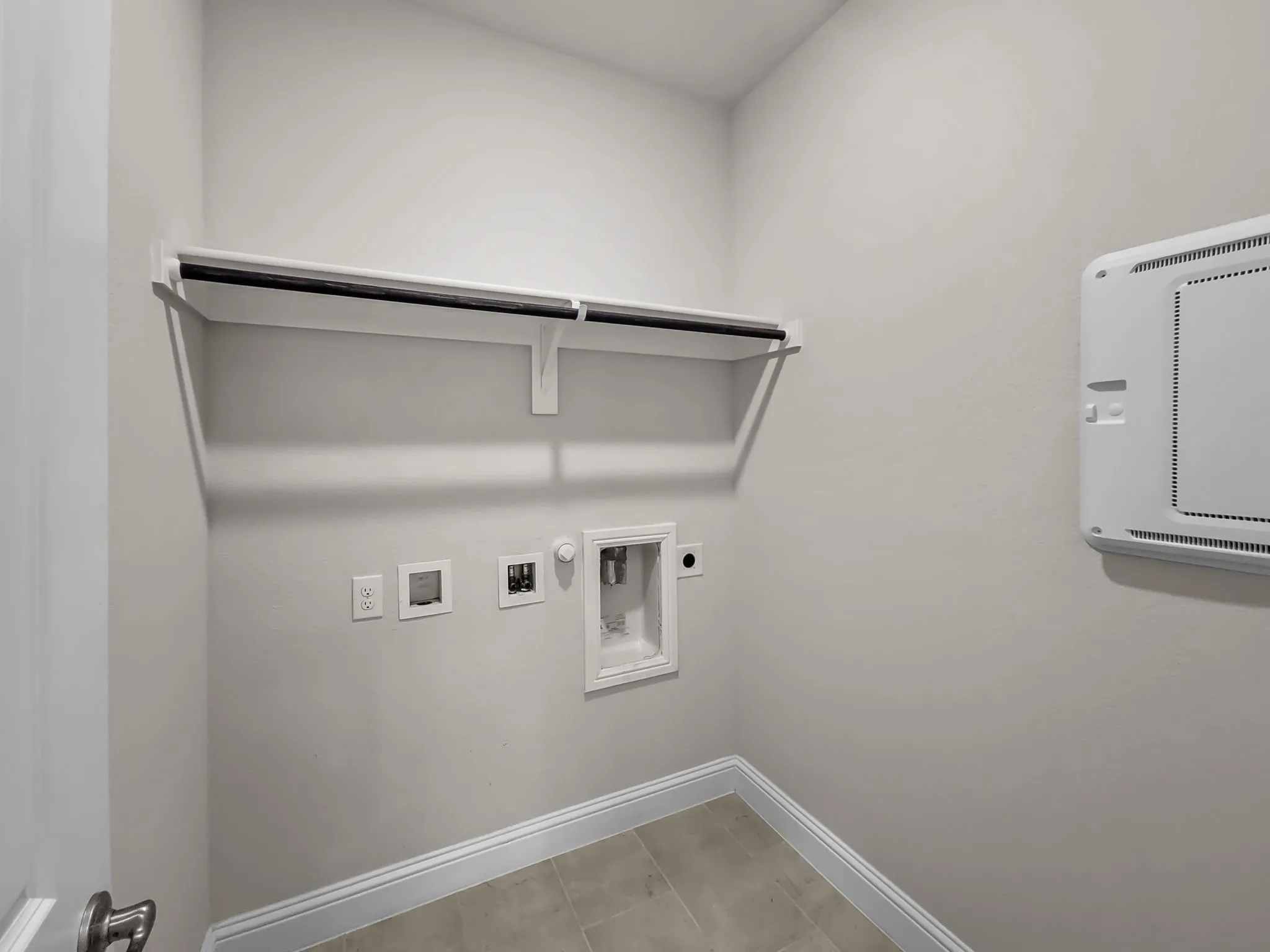 Laundry area with a built-in shelf, hanging rod, and tile flooring