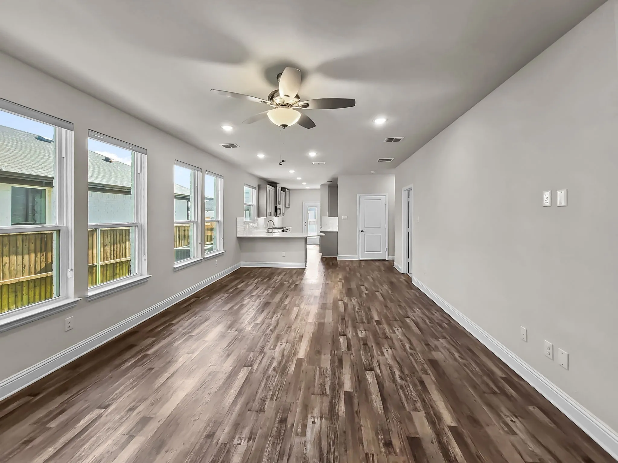 Expansive room featuring wood-finish flooring, multiple windows, a ceiling fan, recessed lighting, and a kitchen with a white countertop
