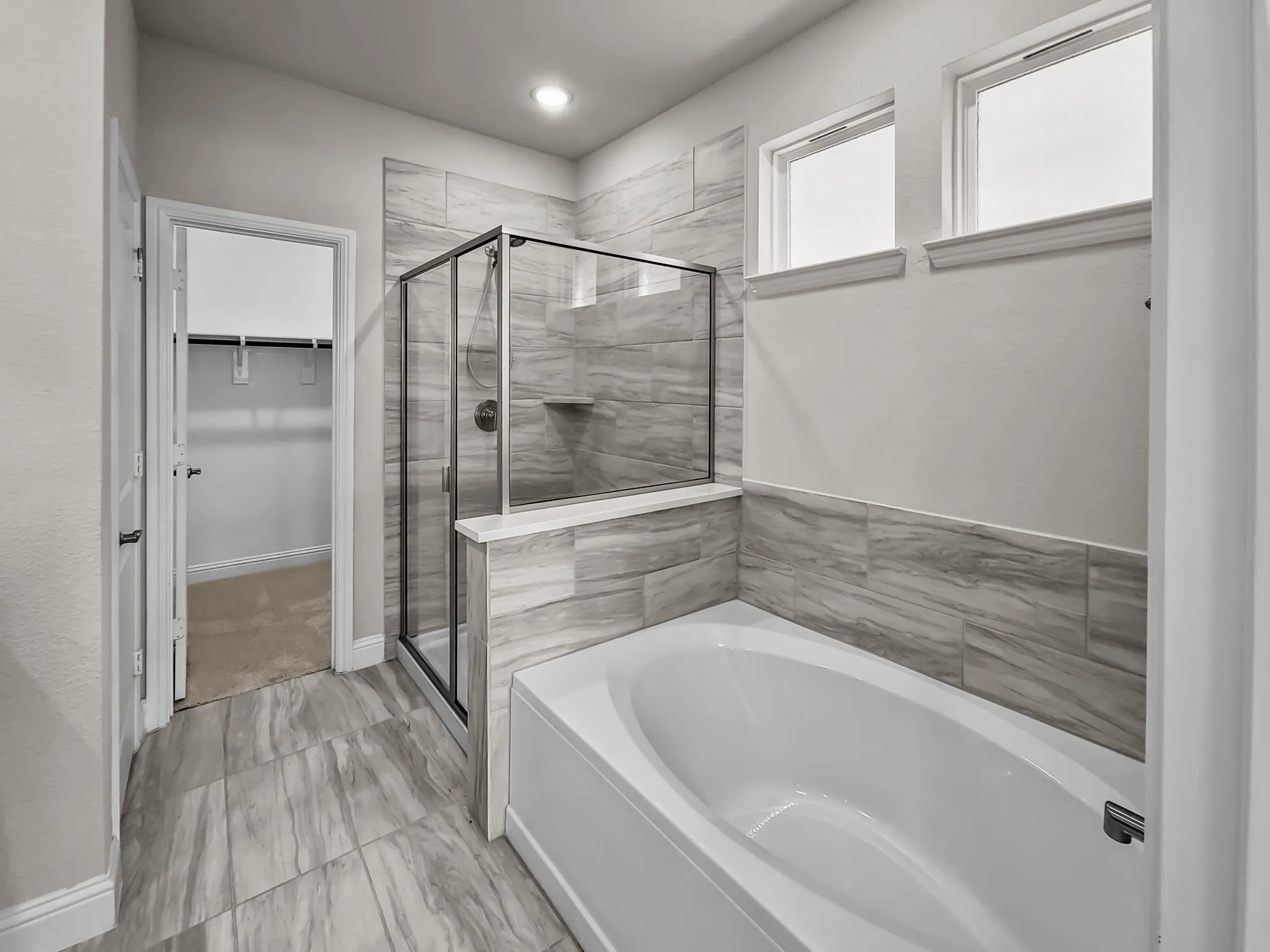 Built-in soaking tub, glass-enclosed shower, tiled walls, large format floor tiling, and dual high windows