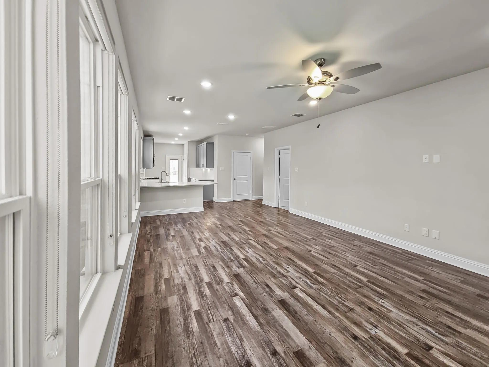 Expansive wood-finish flooring throughout, bright recessed lighting, and a ceiling fan with integrated lighting