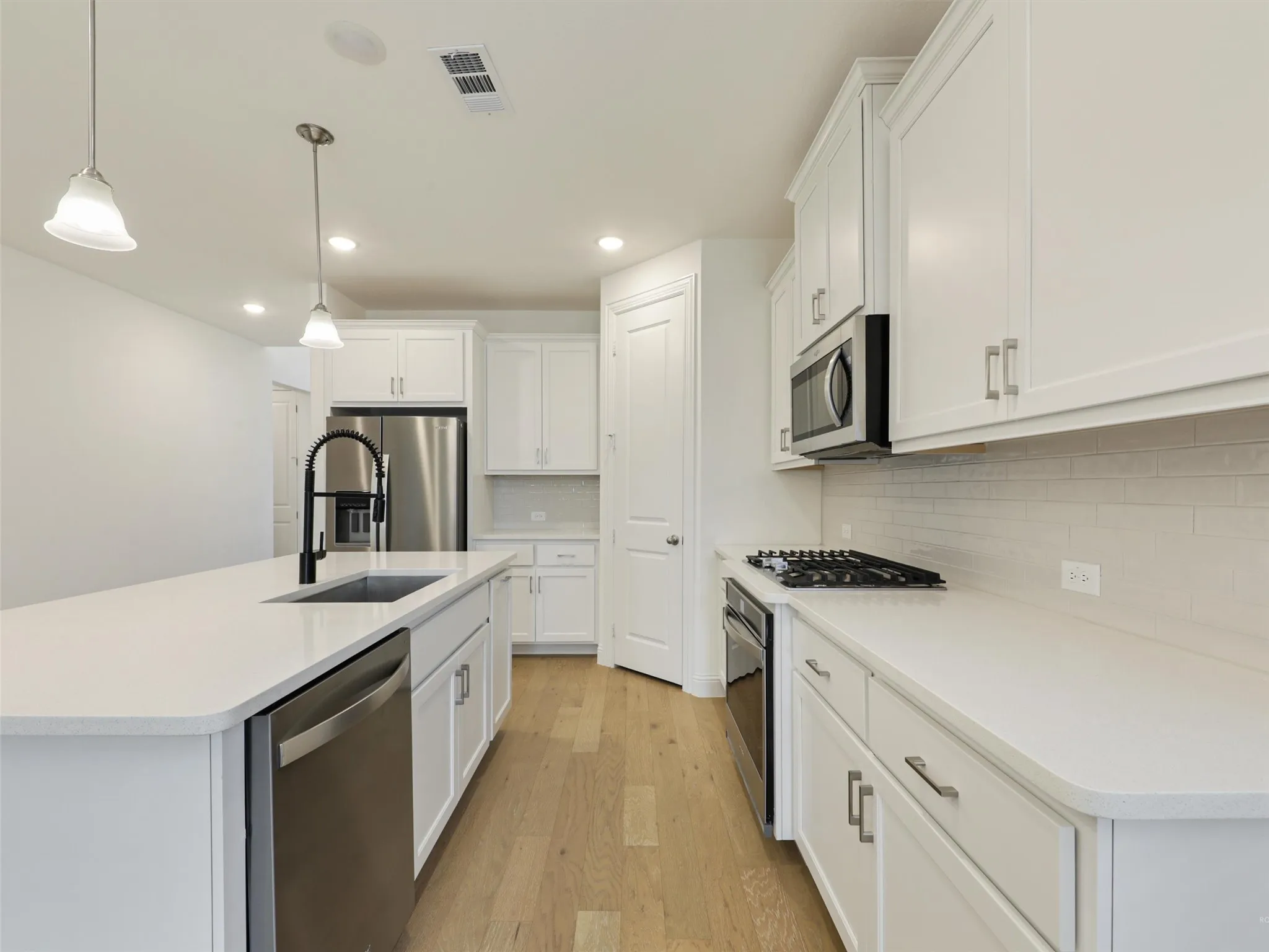 Kitchen with white cabinetry, stainless steel appliances, a center island with a sink, and wood-finish flooring