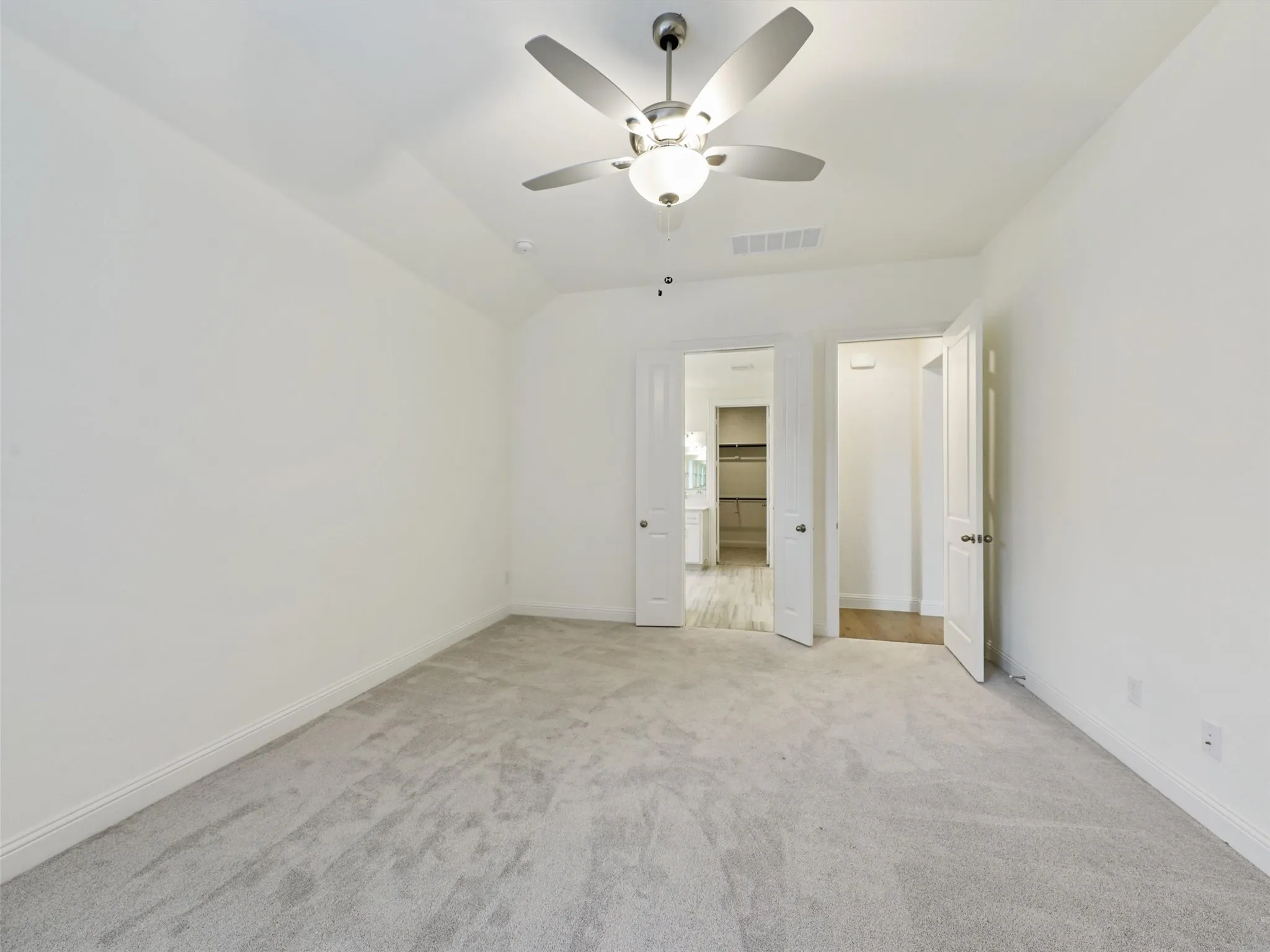 Spacious bedroom with neutral carpeting, ceiling fan with integrated lighting, and dual closet access