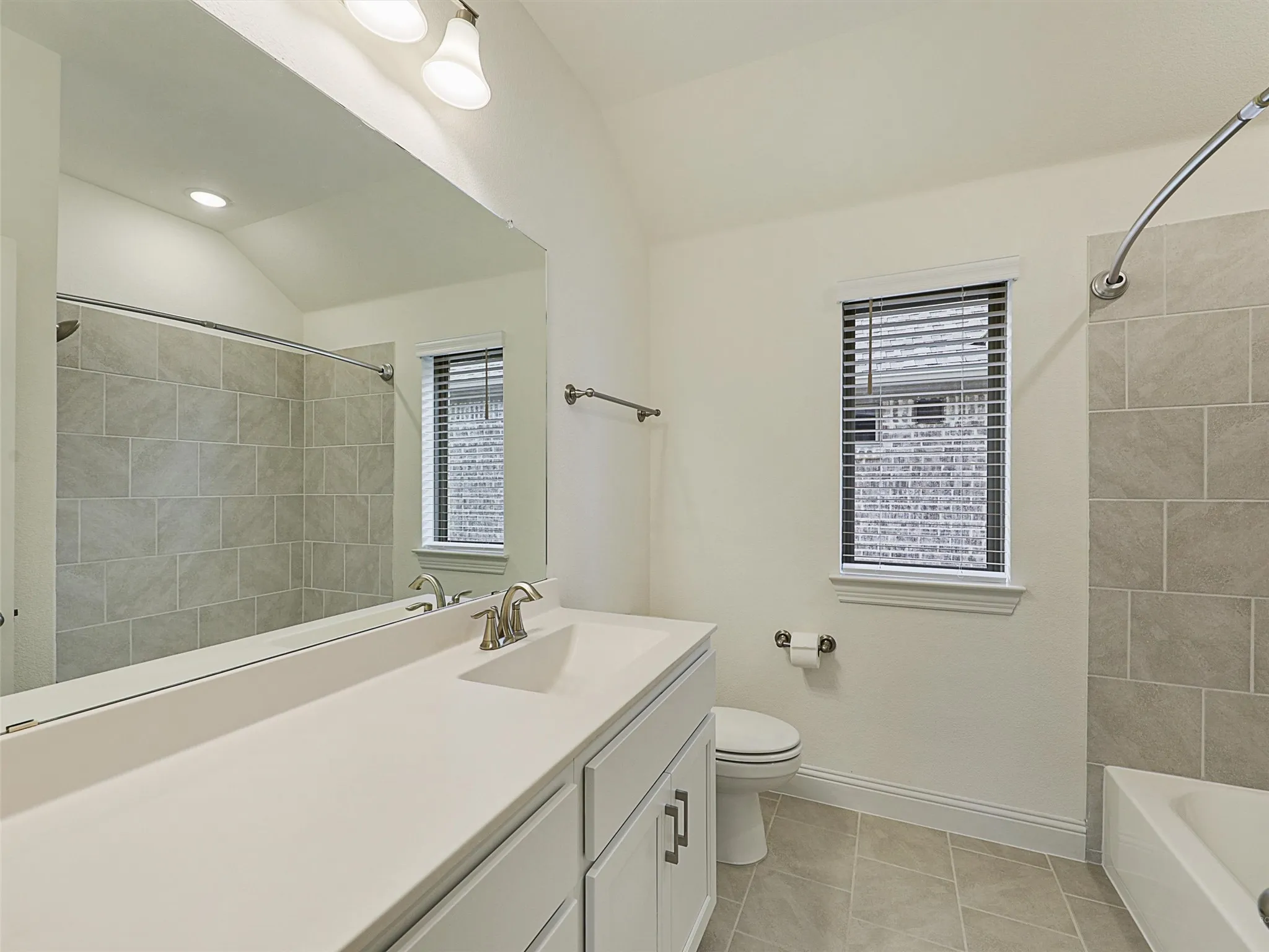 Vanity with a single sink and white cabinetry, a large wall-mounted mirror, a tiled shower/tub combination, tiled flooring, and a window with blinds