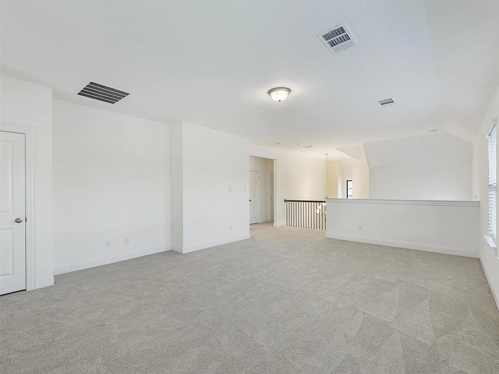Spacious loft area with light gray carpeting, white walls, and a semi-flush ceiling light fixture