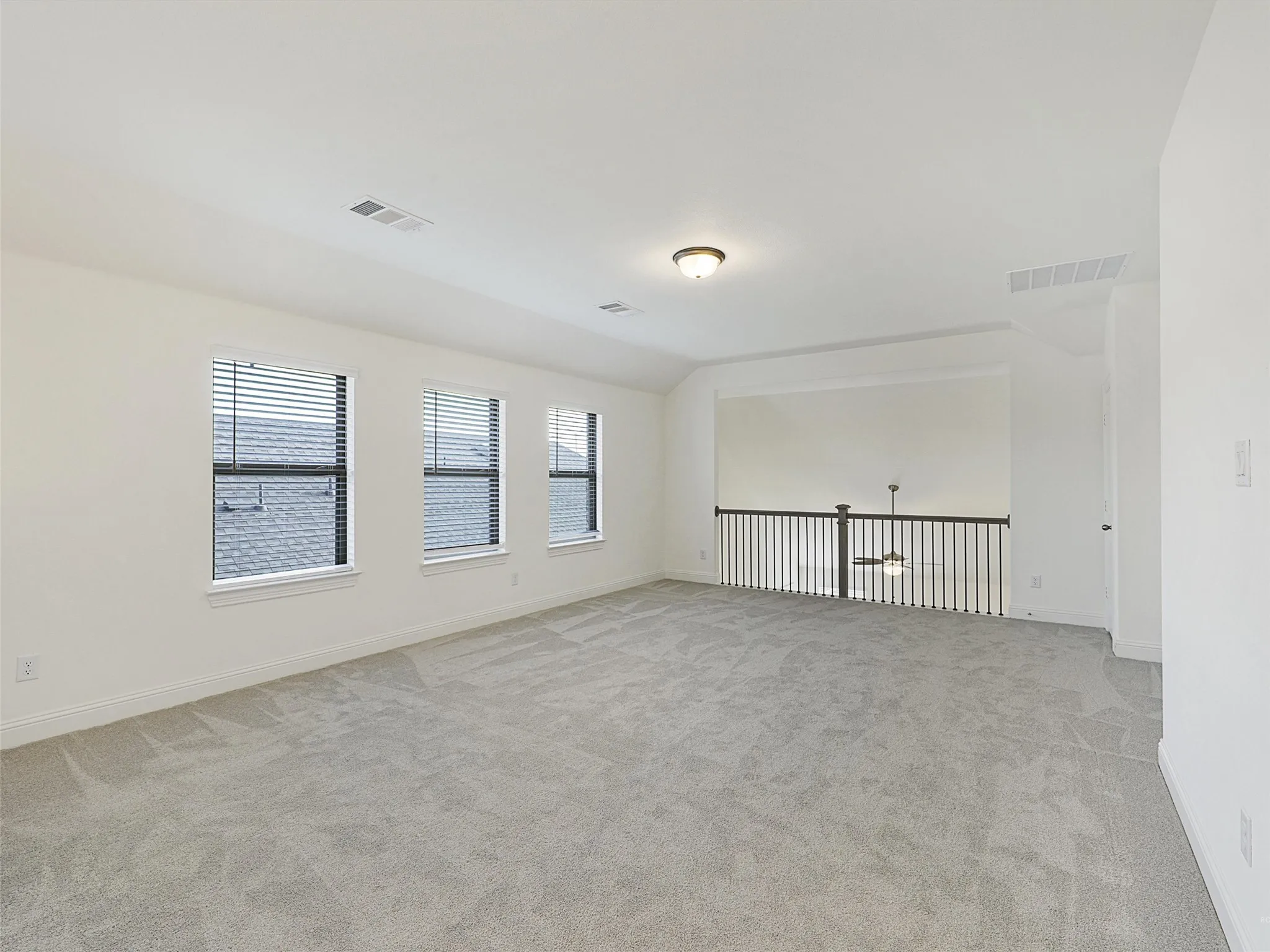 Spacious carpeted room featuring three windows with blinds and a railing overlooking a lower level