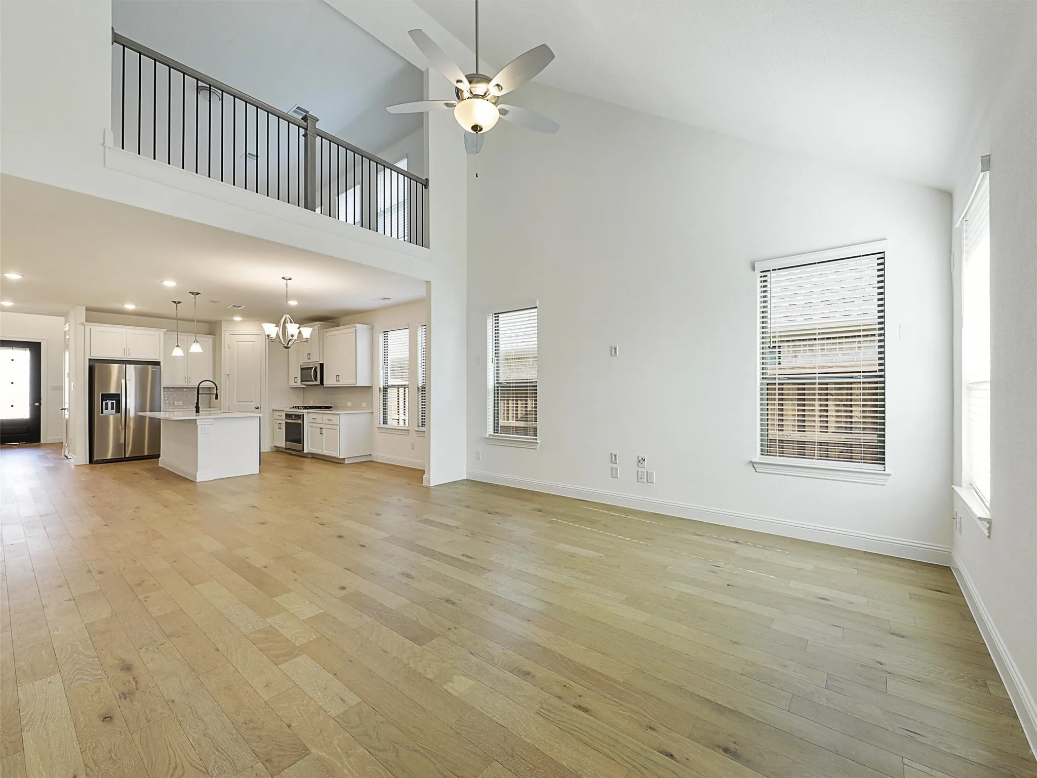 Vaulted ceiling with a ceiling fan, light wood-finish flooring, white kitchen cabinetry, kitchen island with a sink, and stainless steel appliances
