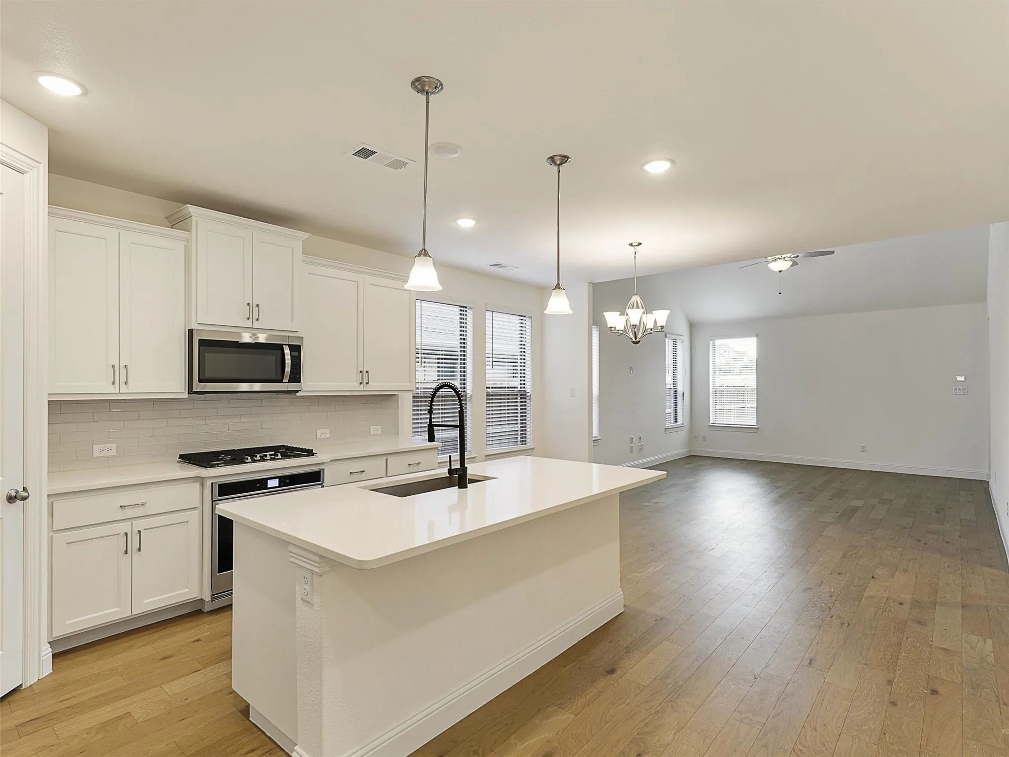 Kitchen island with pendant lighting, white cabinetry, integrated stainless steel appliances, and wood-finish flooring throughout