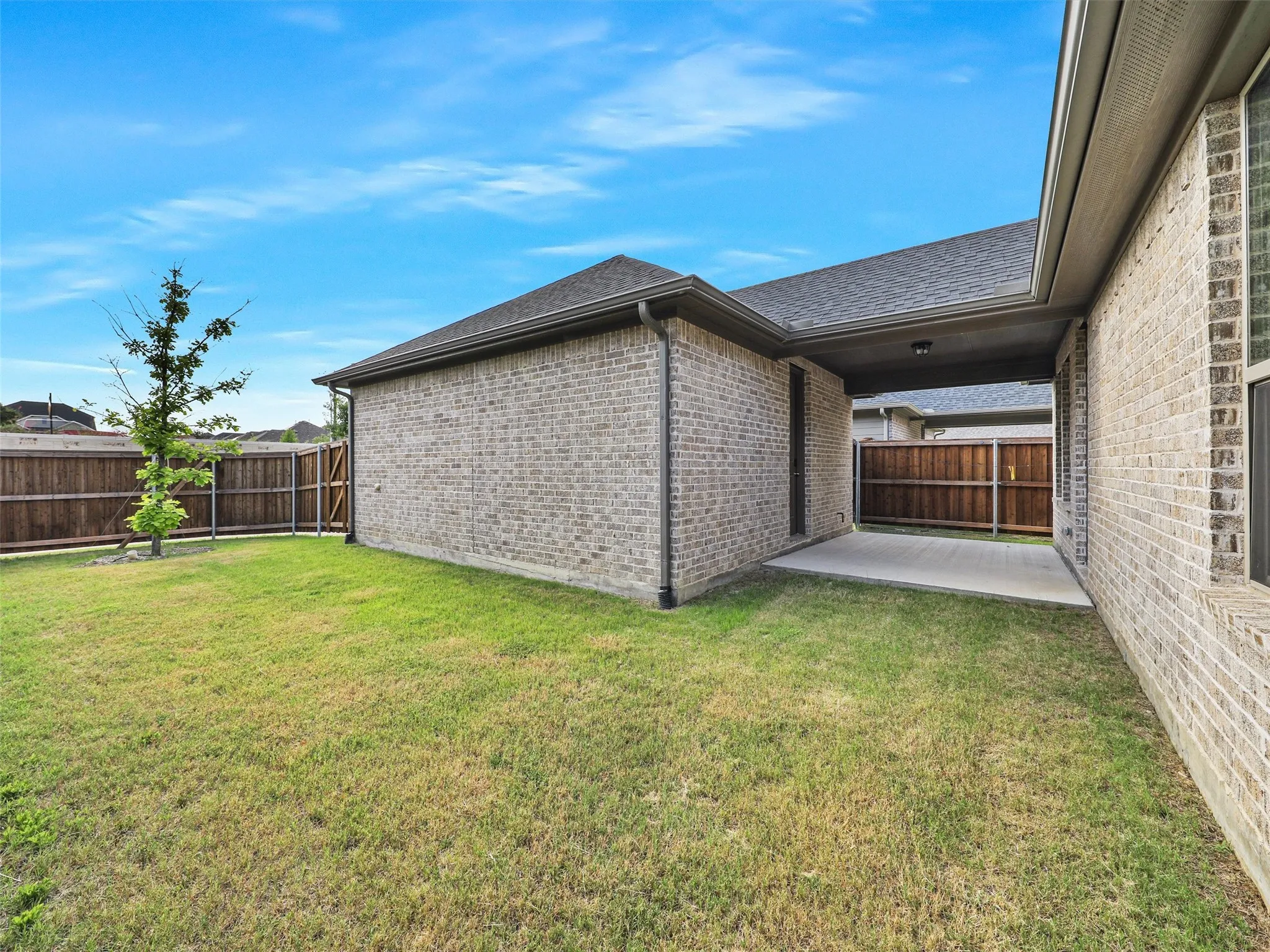 Expansive green lawn, a covered patio, brick exterior, and a wood privacy fence