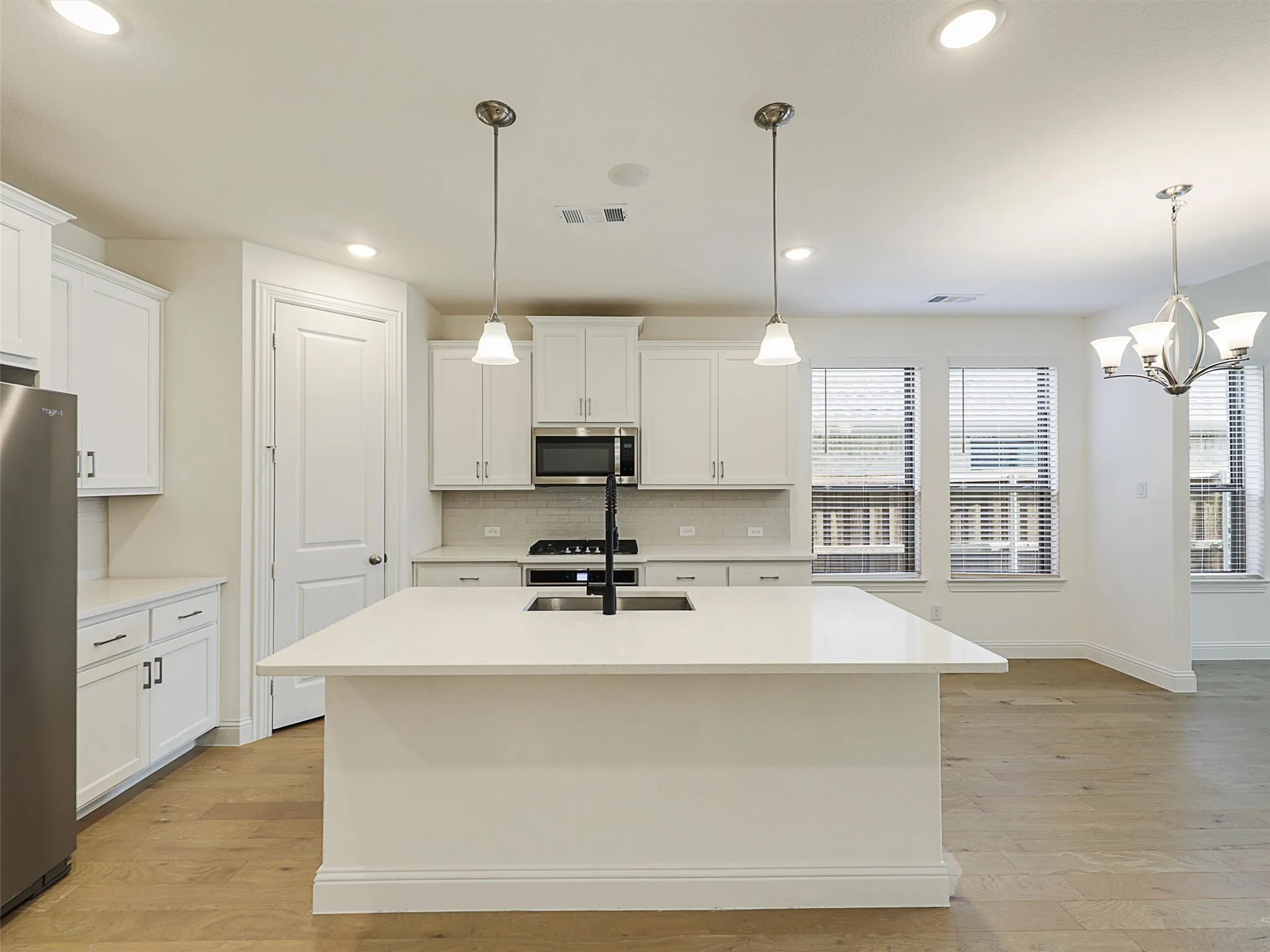 Kitchen with white cabinetry, stainless steel appliances, a center island with sink, and wood-finish flooring