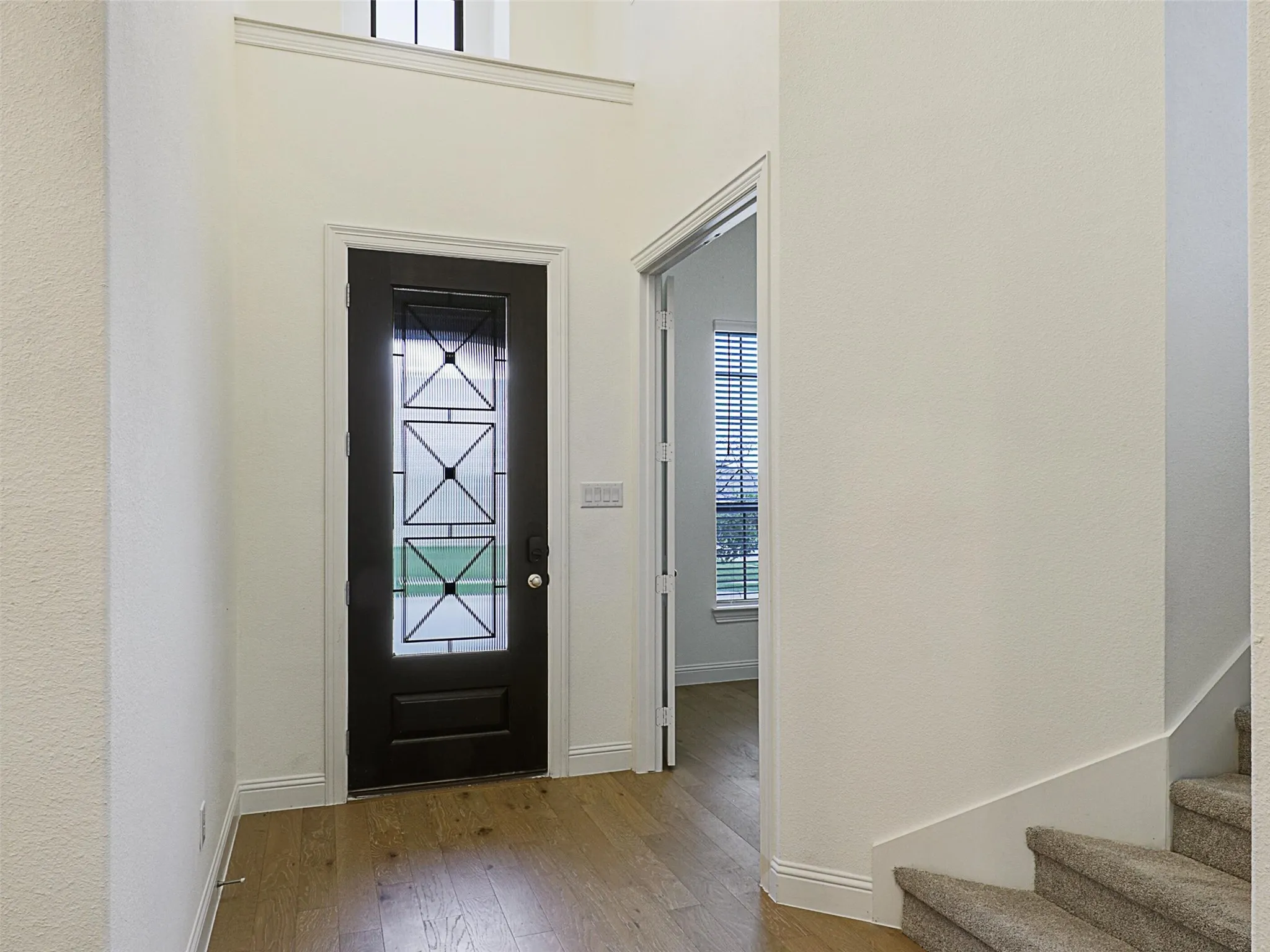 Dark entry door with decorative glass inserts, wood-finish flooring, and a carpeted staircase
