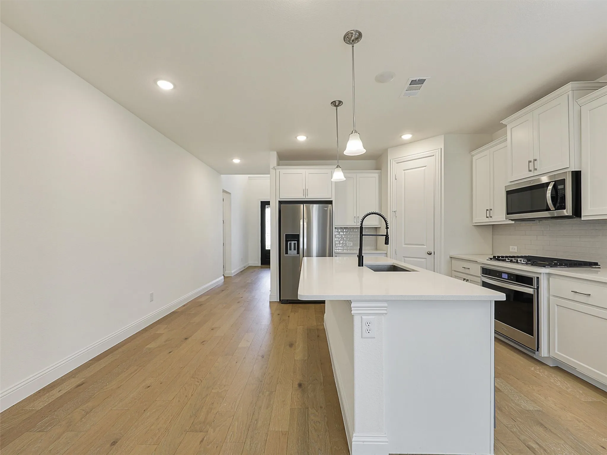 Kitchen featuring white cabinetry, quartz countertops, stainless steel appliances, and a central island with an undermount sink and matte black faucet