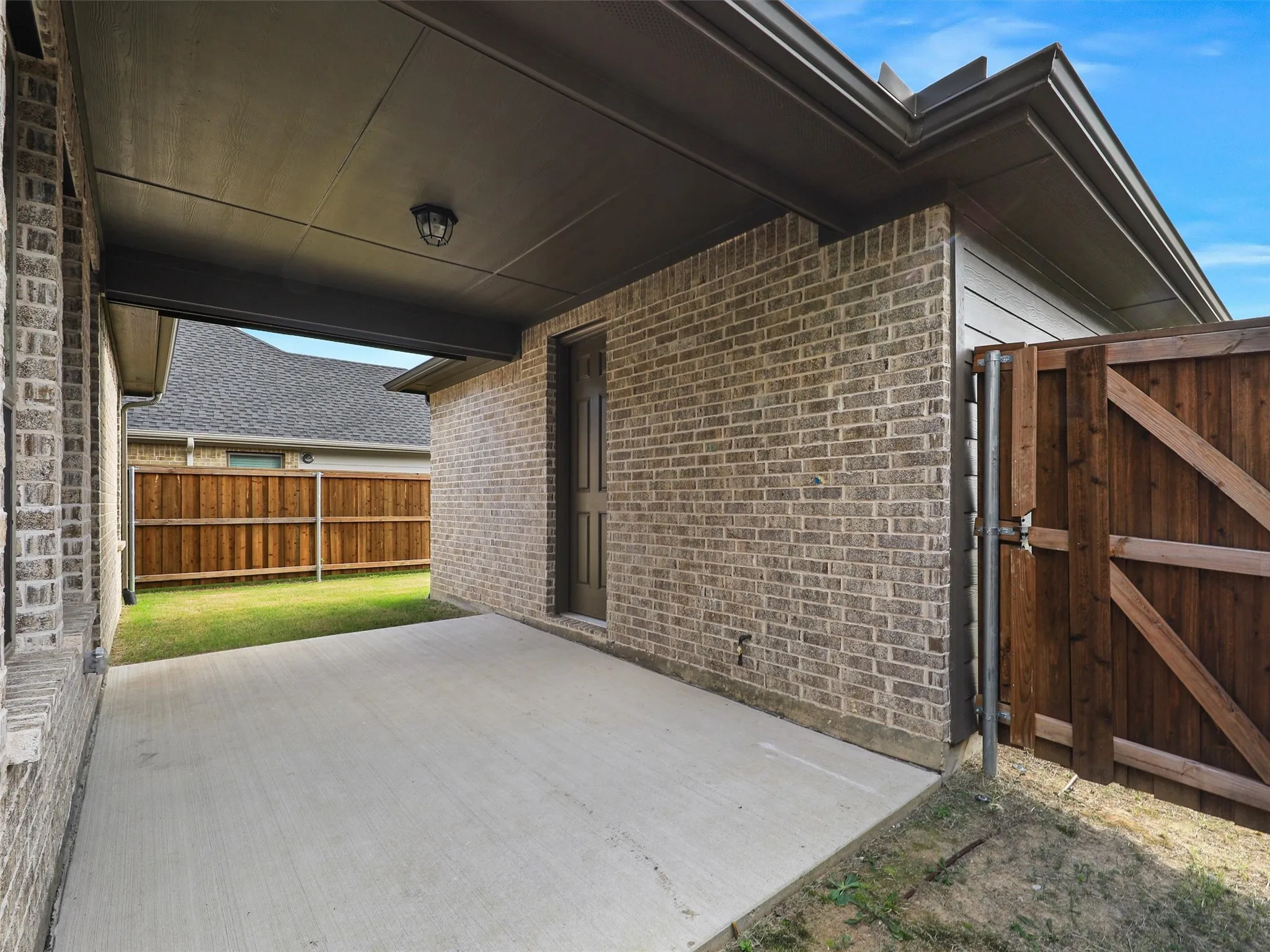 Covered concrete patio with brick exterior and dark wood fencing