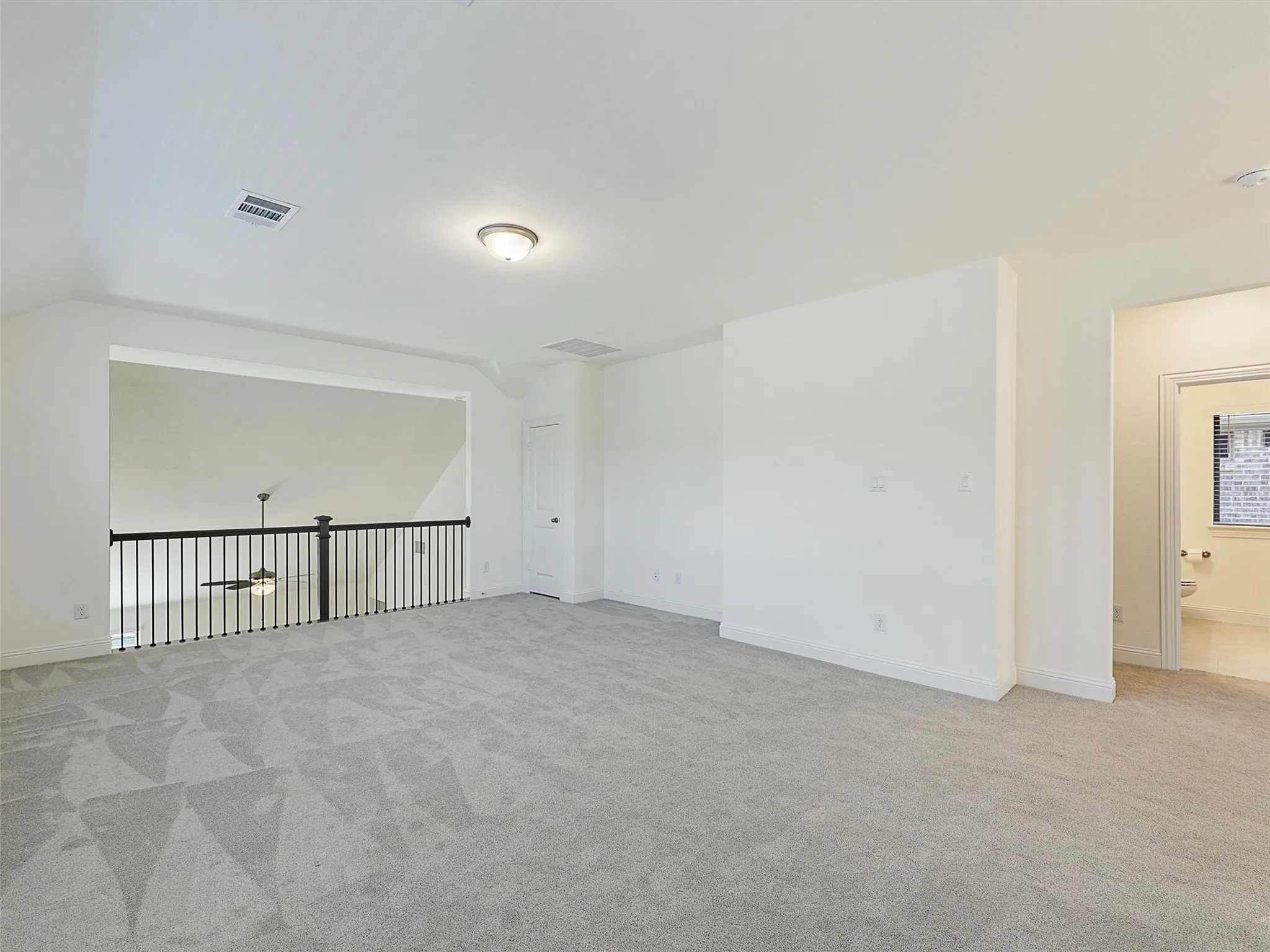 Expansive carpeted area with a white wall finish, an overhead flush mount light, and an open railing overlooking a lower level