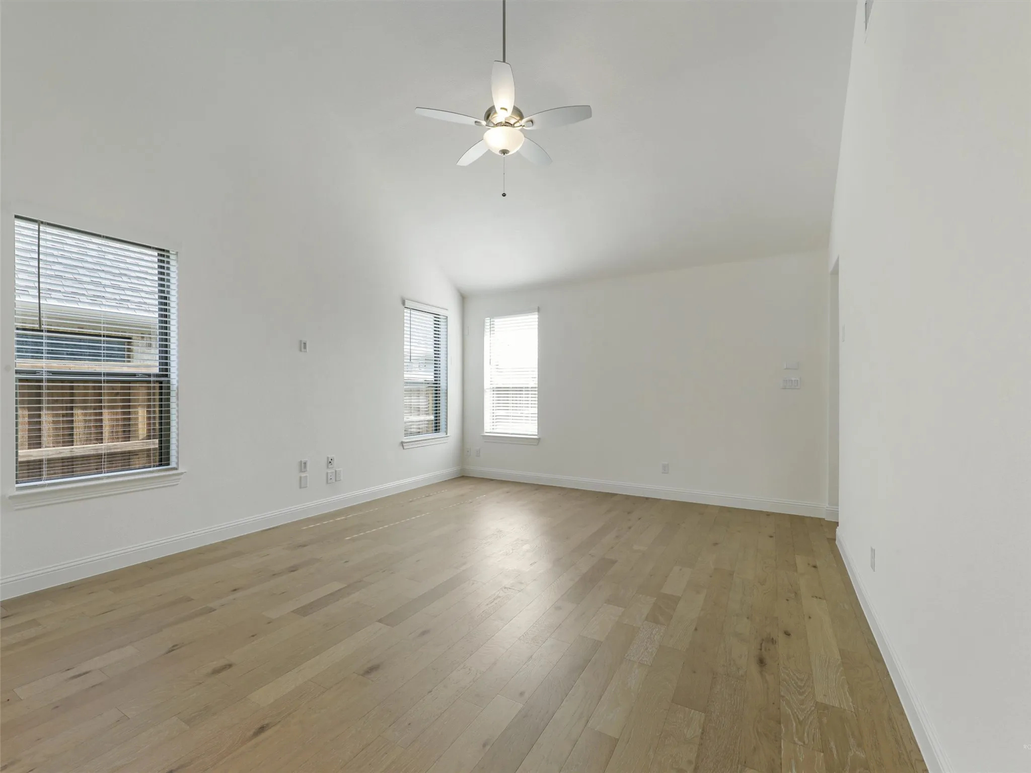 Vaulted ceiling, ceiling fan, wood-finish flooring, multiple windows with blinds, white walls