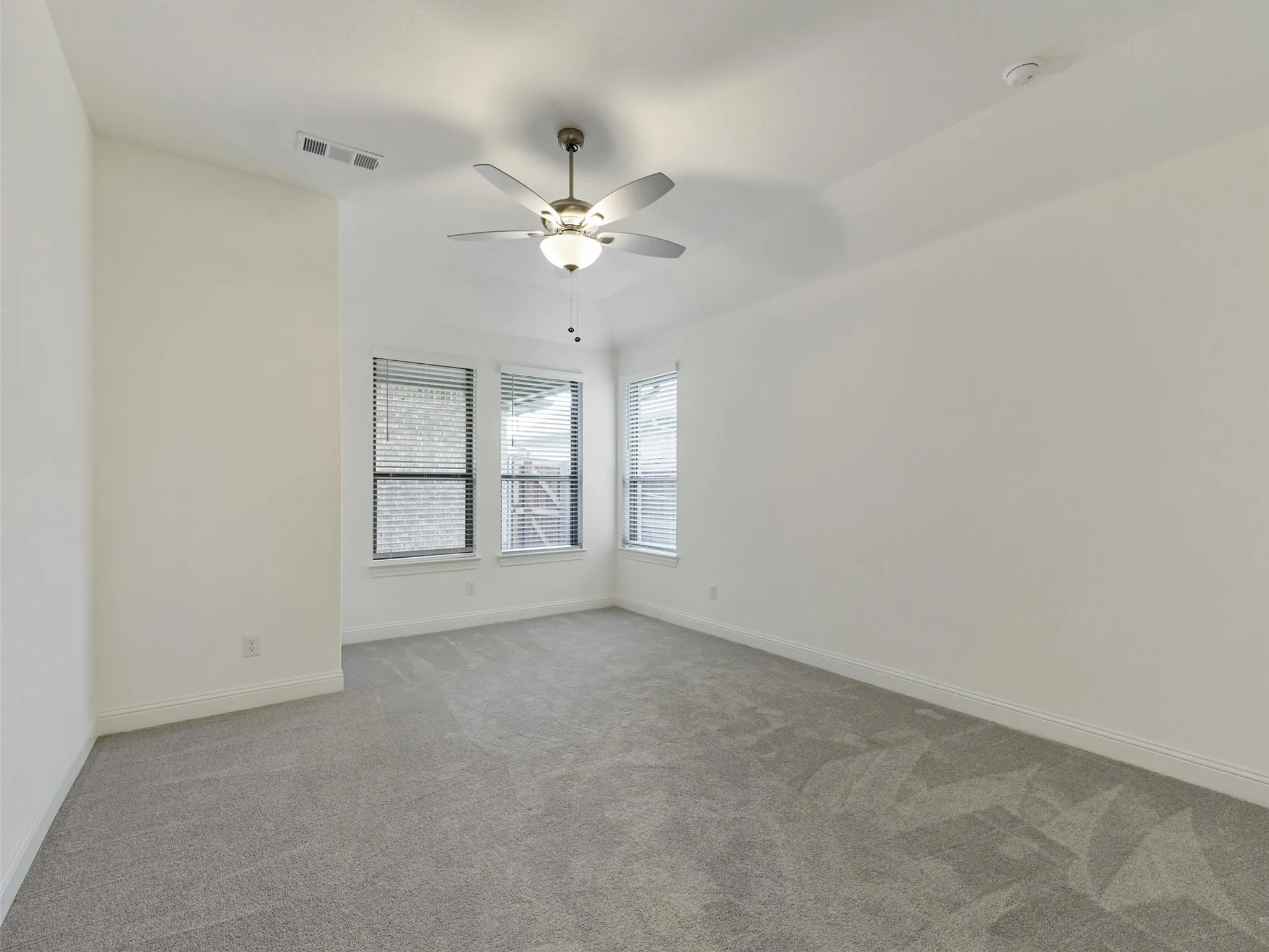 Carpeted room featuring multiple windows, a ceiling fan with integrated lighting, and neutral wall tones