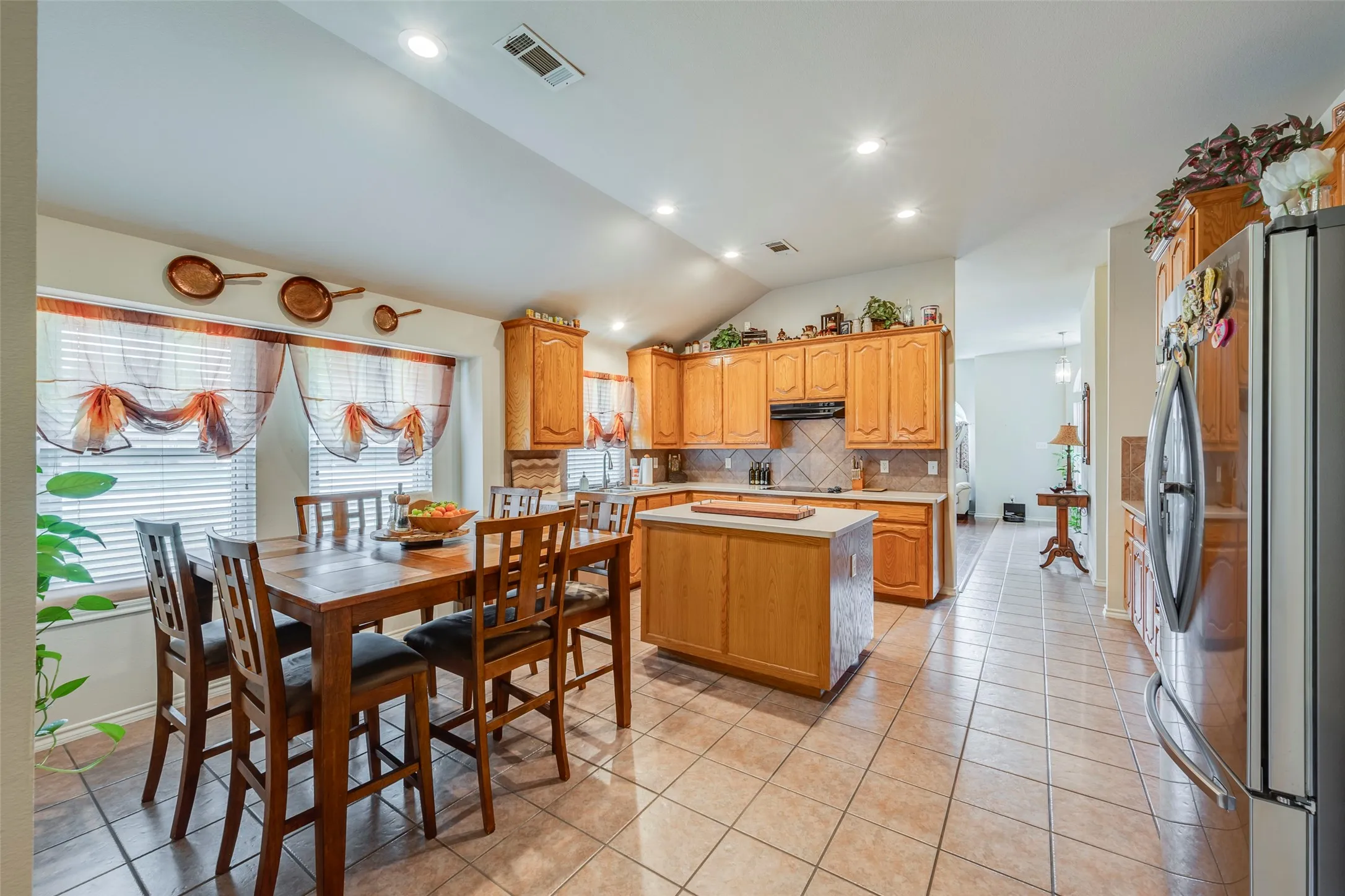 Vaulted ceiling kitchen featuring wood cabinetry, a center island with a light-toned countertop, tile flooring, and integrated recessed lighting