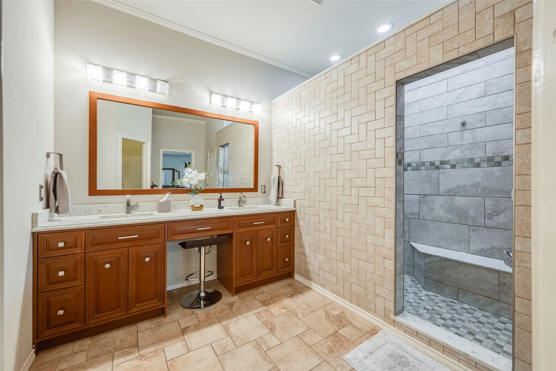 Double vanity with wood-finish cabinetry, countertop, and dual sinks, Spa-like walk in shower with seating and body sprays