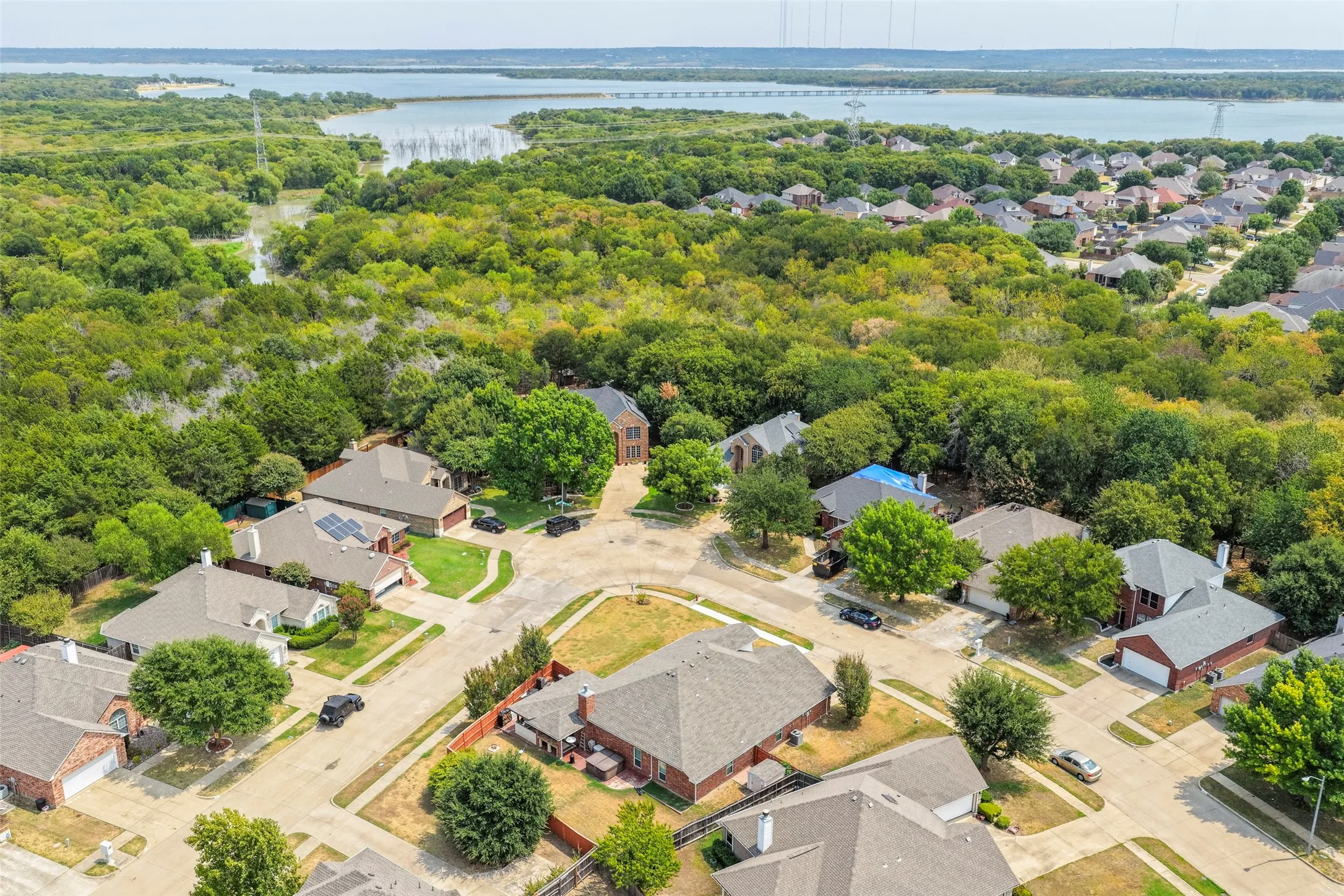 Aerial perspective showcasing a residential neighborhood with surrounding mature trees and a Lake in the background