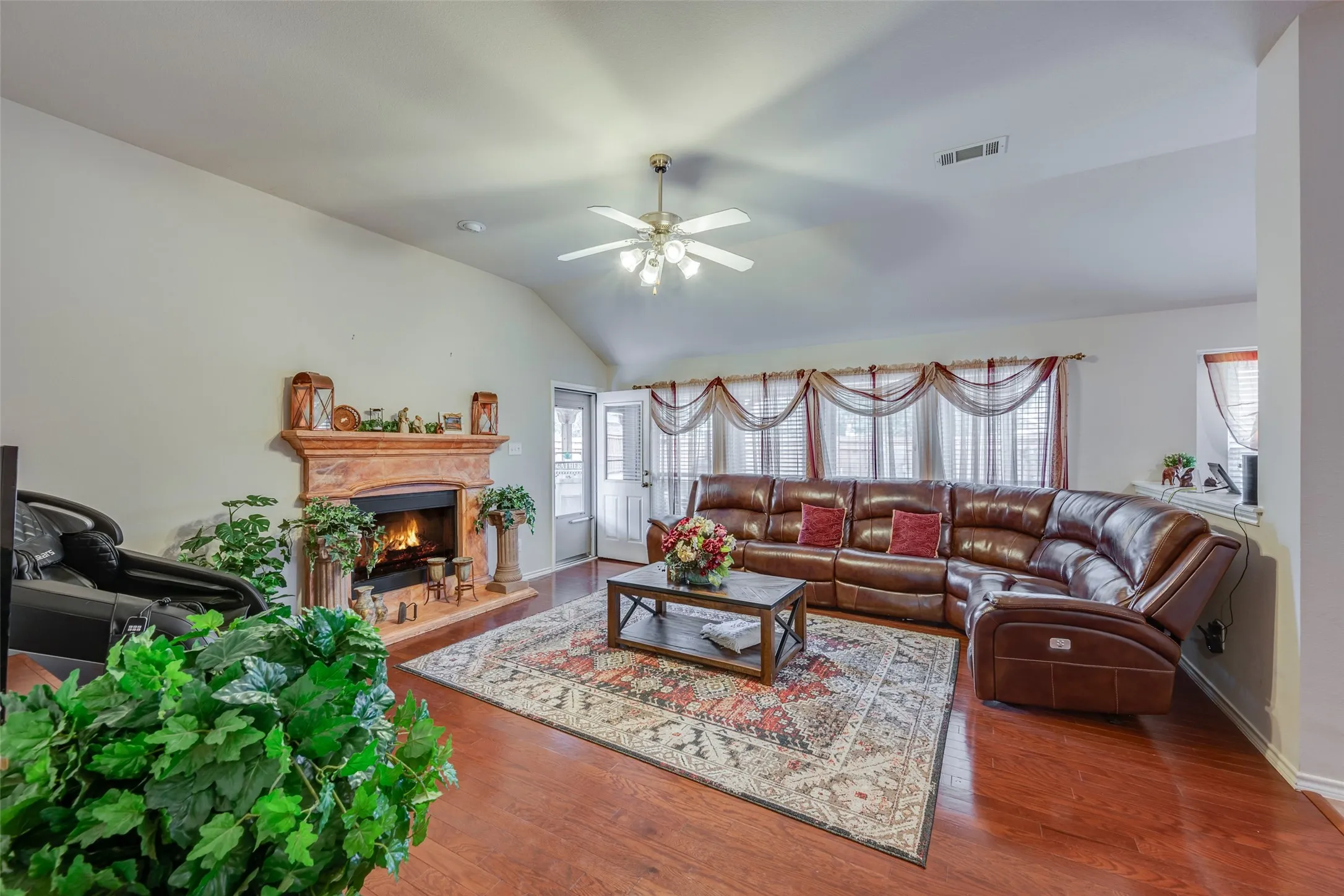 Vaulted ceilings, a built-in fireplace with a decorative mantel, wood-finish flooring, and a ceiling fan with light fixture