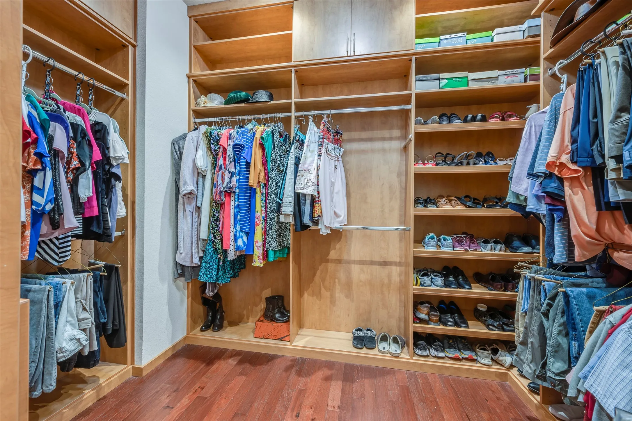 Custom-built closet system featuring extensive wood-finish shelving, multiple hanging rods, and integrated storage