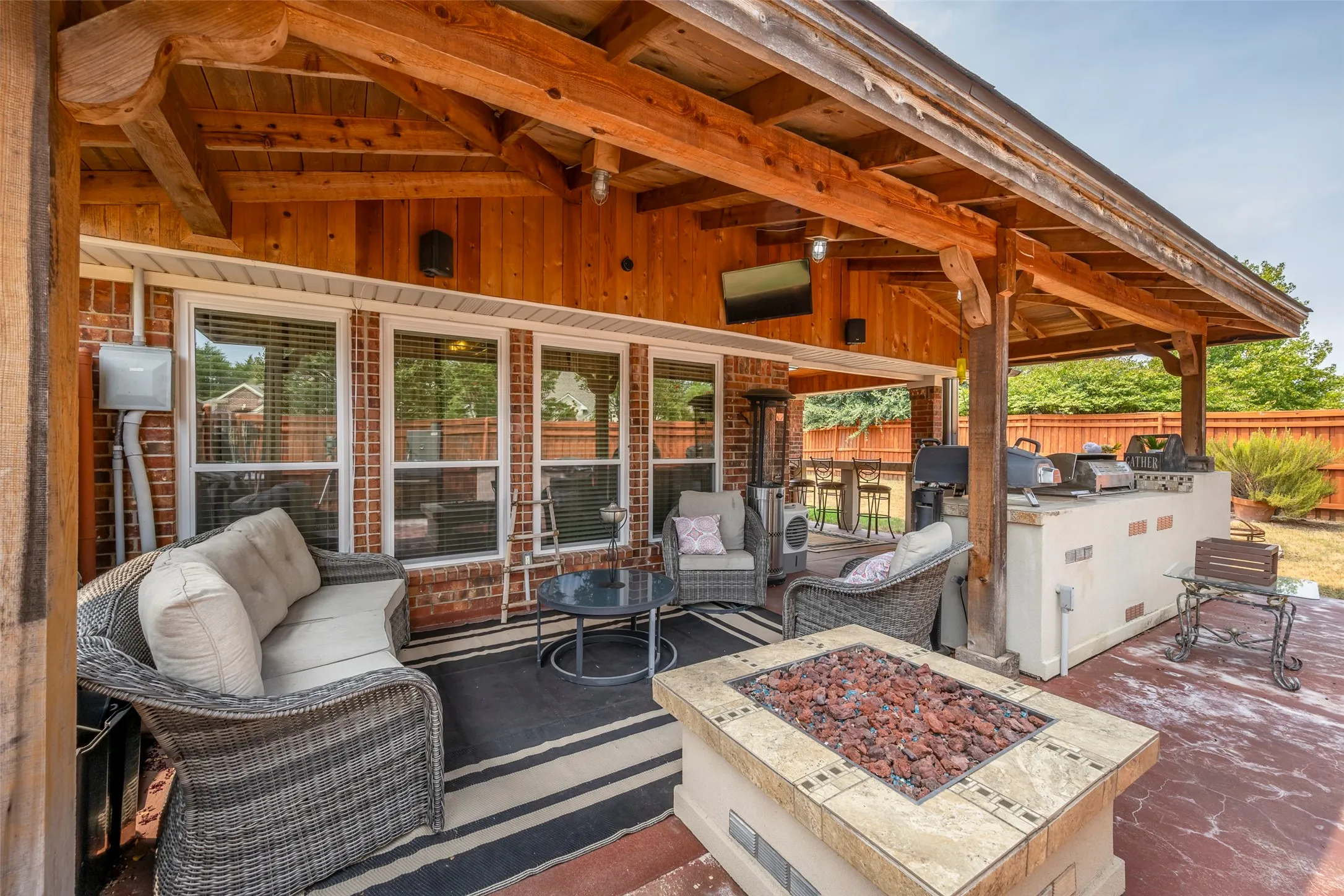 Covered outdoor patio with exposed timber beams, a built-in outdoor kitchen, and a fire pit