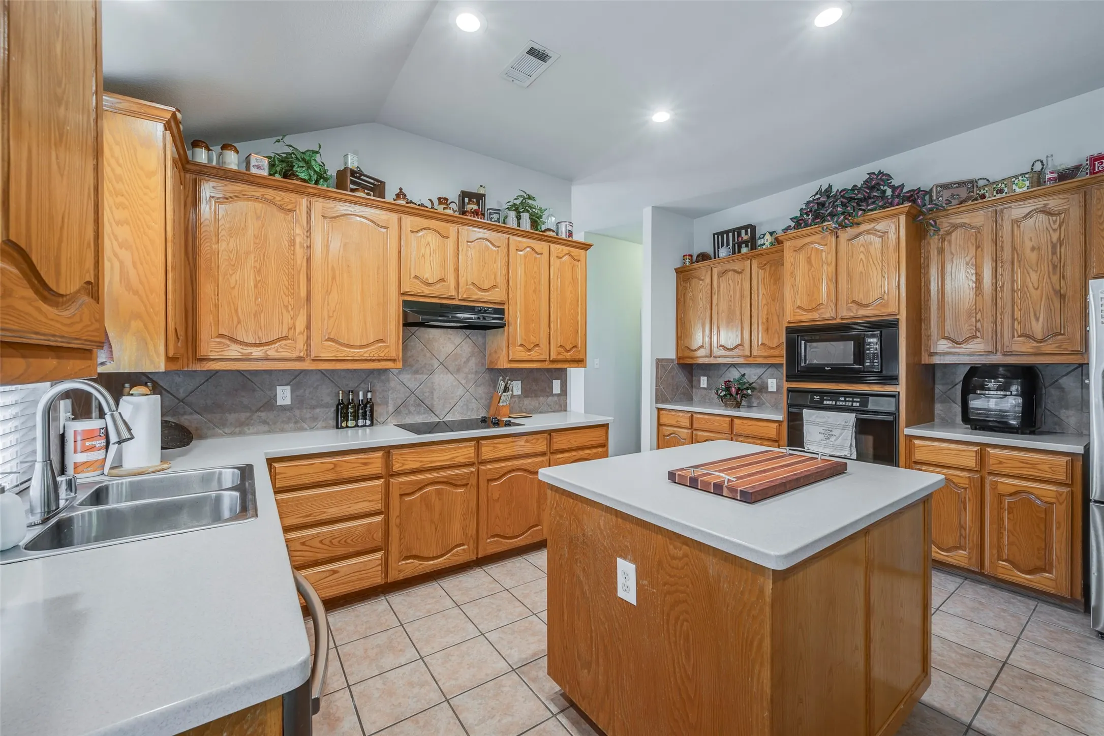 Kitchen featuring wood cabinetry, an integrated cooktop, stainless steel sink, tiled flooring, and a central island