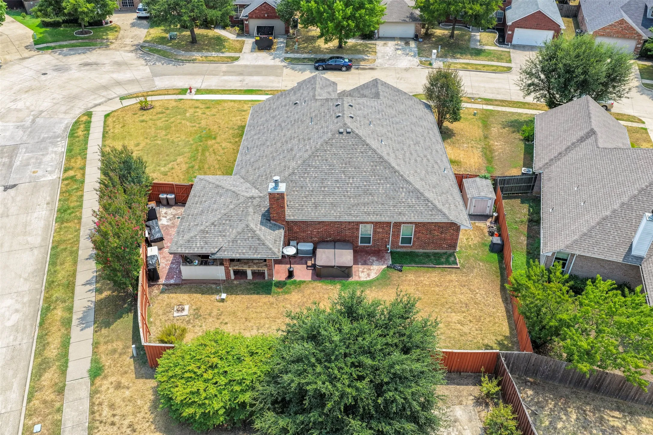 Fenced backyard with mature trees, a covered patio area, and a brick exterior