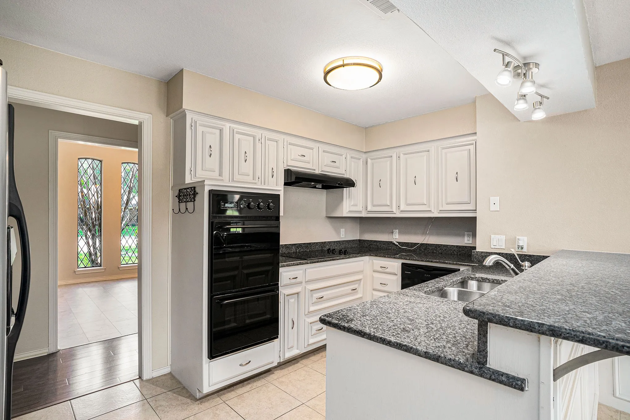 Kitchen with a peninsula, white cabinetry, light tile patterned floors, under cabinet range hood, and refrigerator