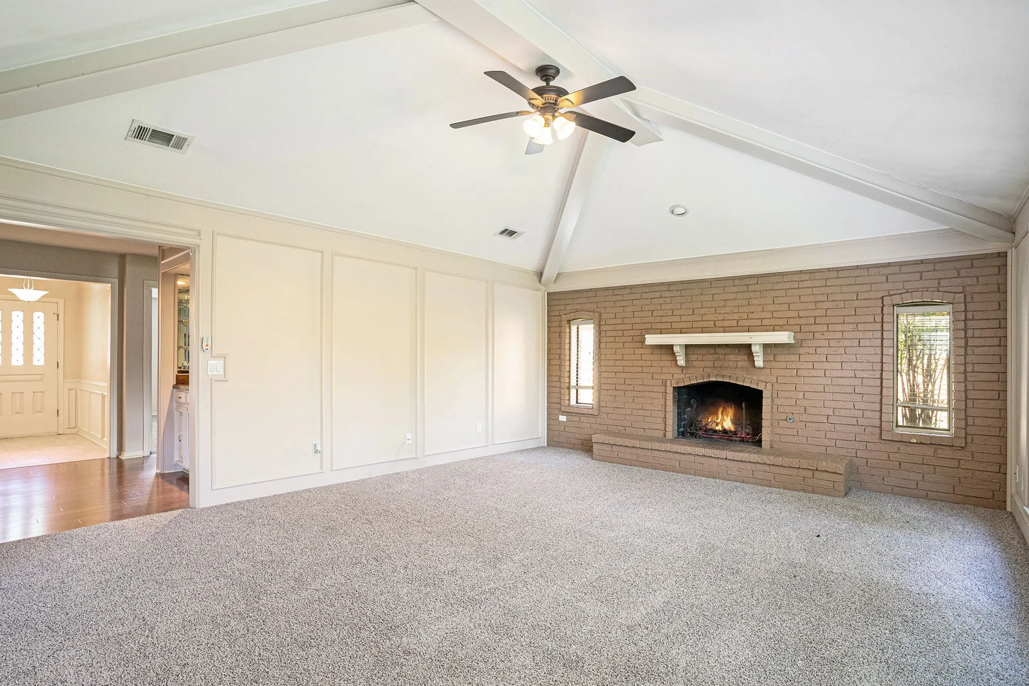 Unfurnished living room featuring healthy amount of natural light, a decorative wall, beam ceiling, high vaulted ceiling, and carpet floors