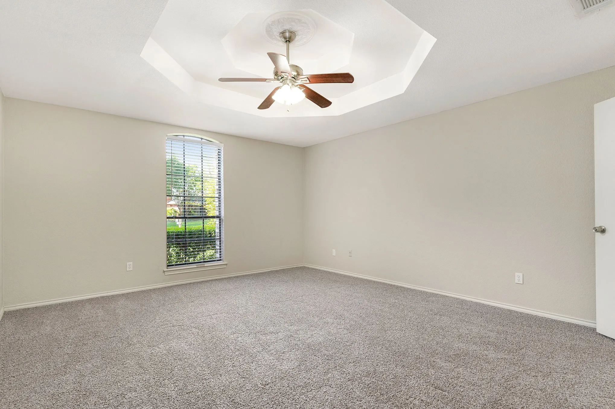 Carpeted empty room with a raised ceiling and ceiling fan