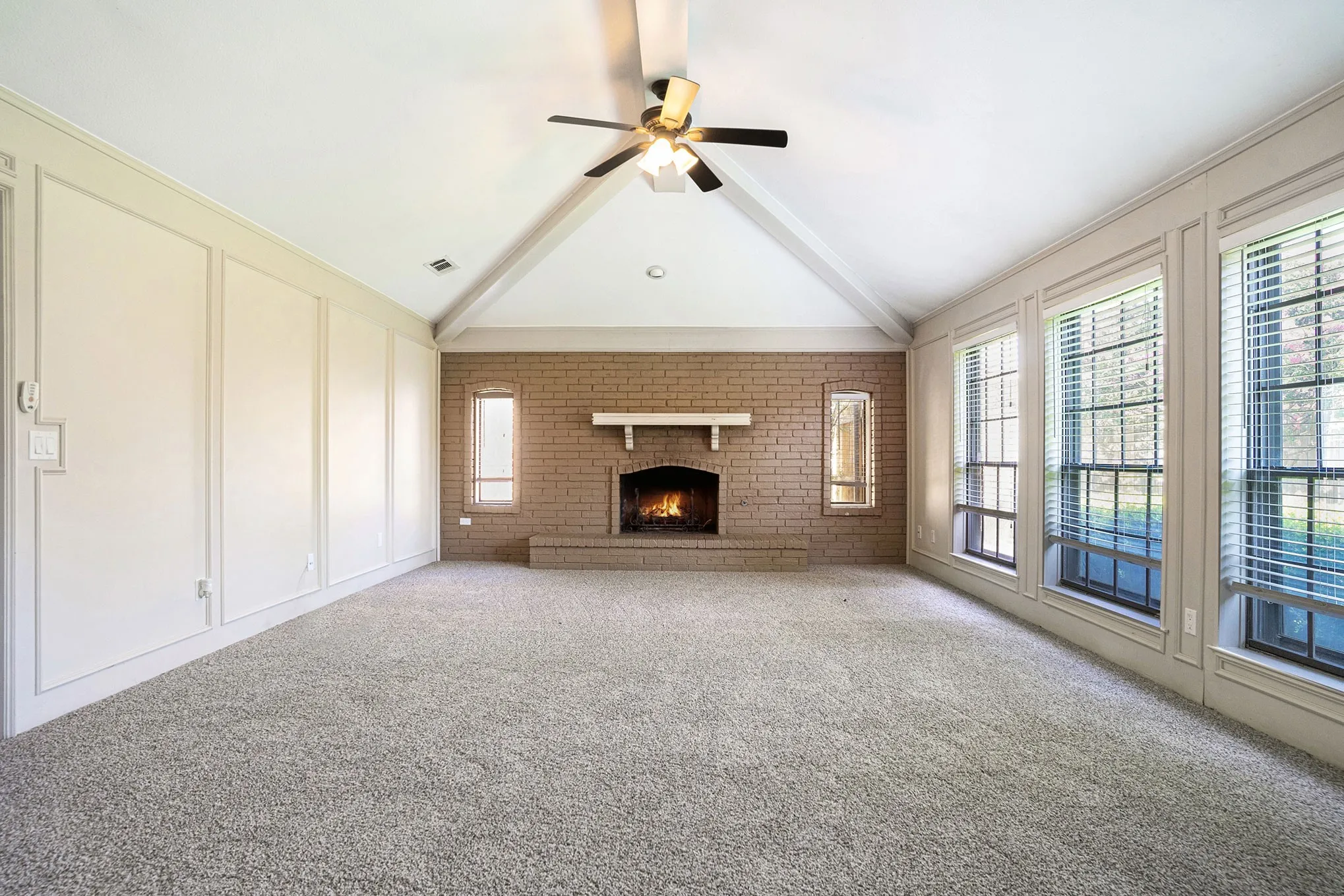 Unfurnished living room featuring a brick fireplace, carpet floors, ceiling fan, and brick wall